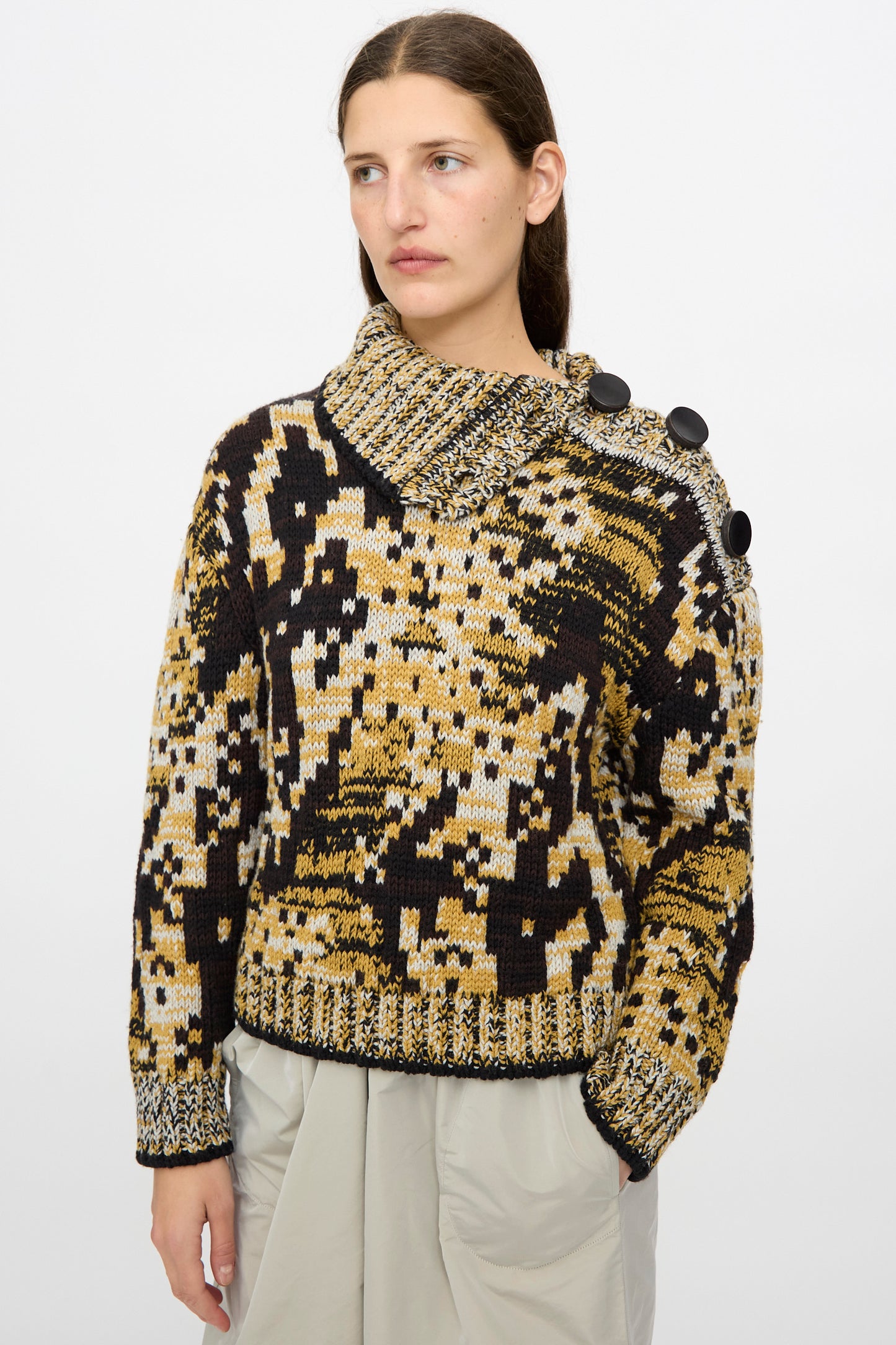 A woman wears the Veronique Leroy Sweater in Sepia, a relaxed fit graphic knit with large black shoulder buttons, paired with a light gray skirt against a plain white background.