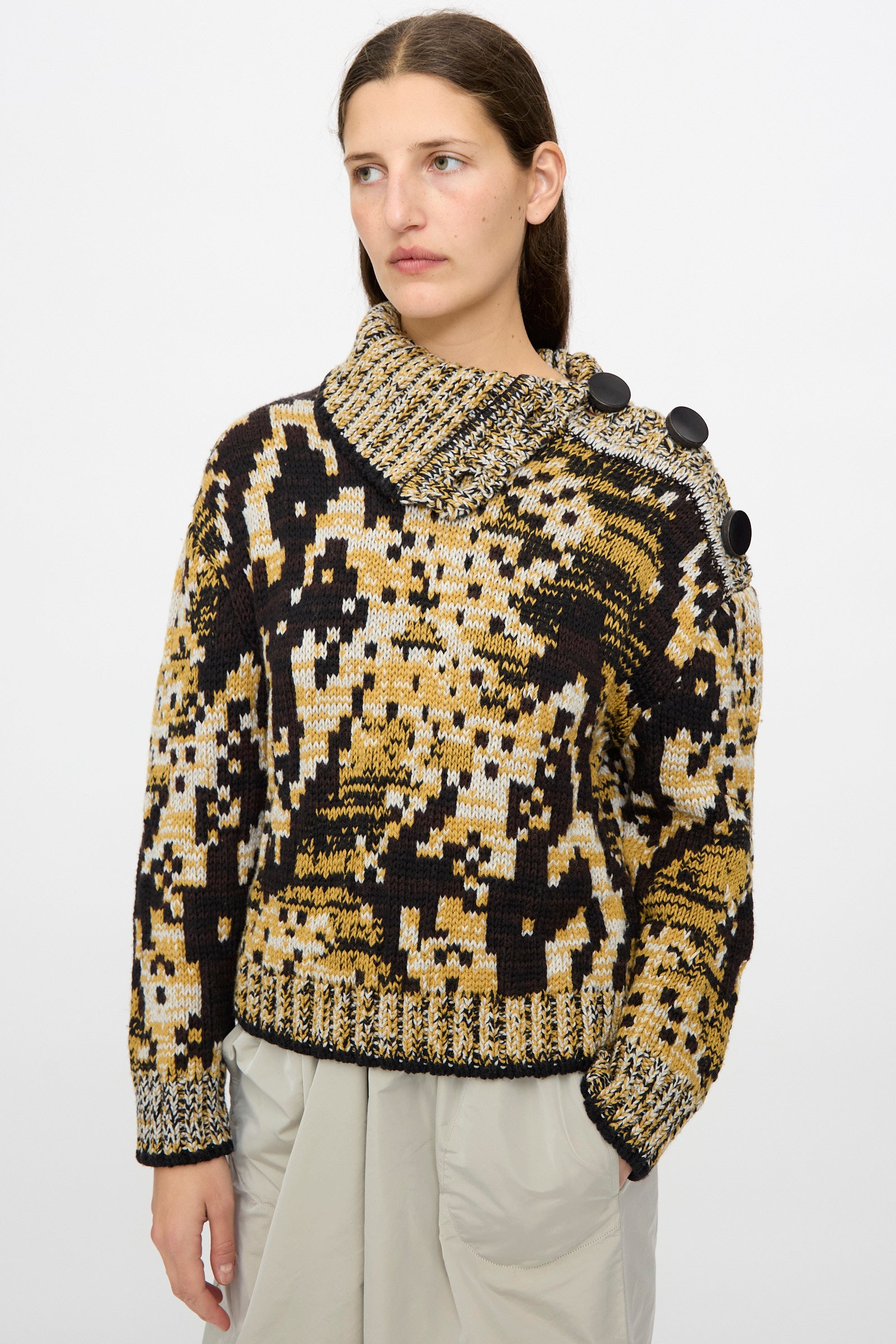 A woman wears the Veronique Leroy Sweater in Sepia, a relaxed fit graphic knit with large black shoulder buttons, paired with a light gray skirt against a plain white background.