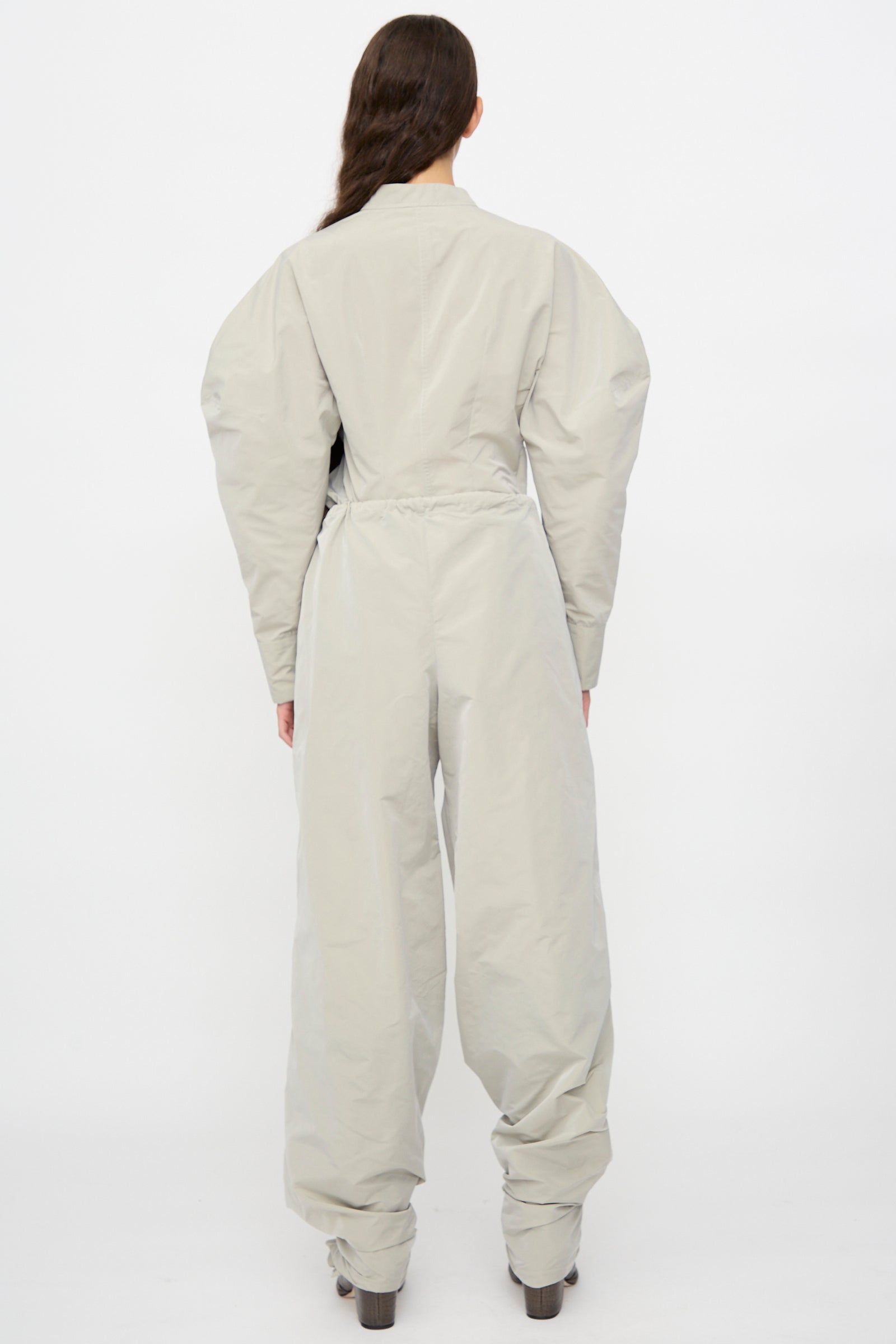 A person stands with their back to the camera, wearing Veronique Leroy’s Tie Pants in Sage paired with dark shoes, shown against a plain white background.