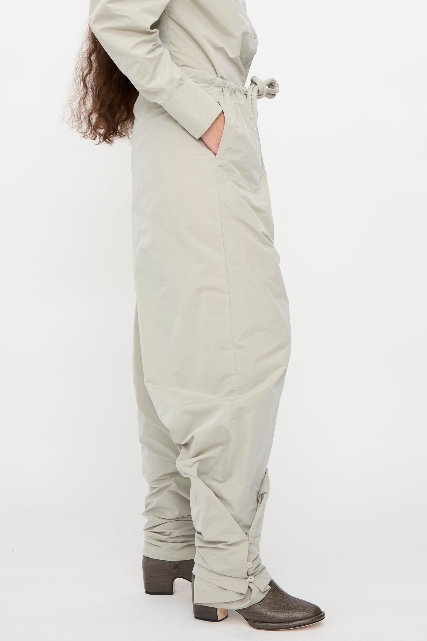 Model wearing Veronique Leroy Tie Pants in Sage, a high-waisted, wide-leg design with hands in pockets, paired with dark heeled ankle boots. Only the lower half of the body is visible.