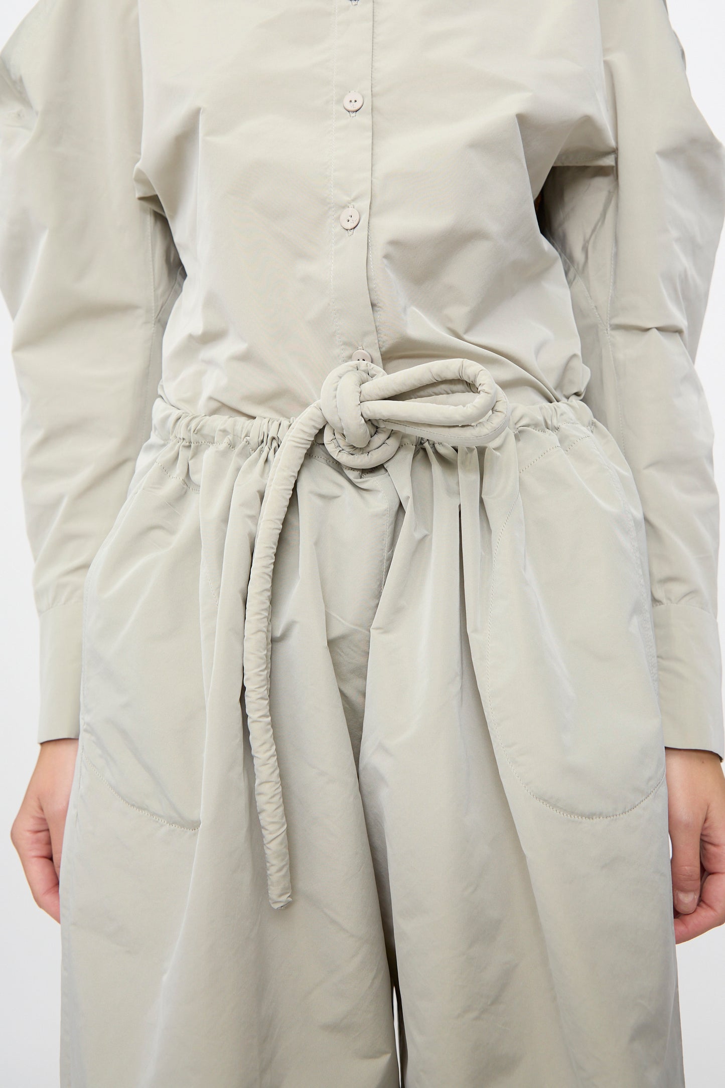 A person wears Veronique Leroy Tie Pants in Sage—high-waisted, wide-leg pants with a knotted fabric belt at the waist, crafted from lightweight taffeta.