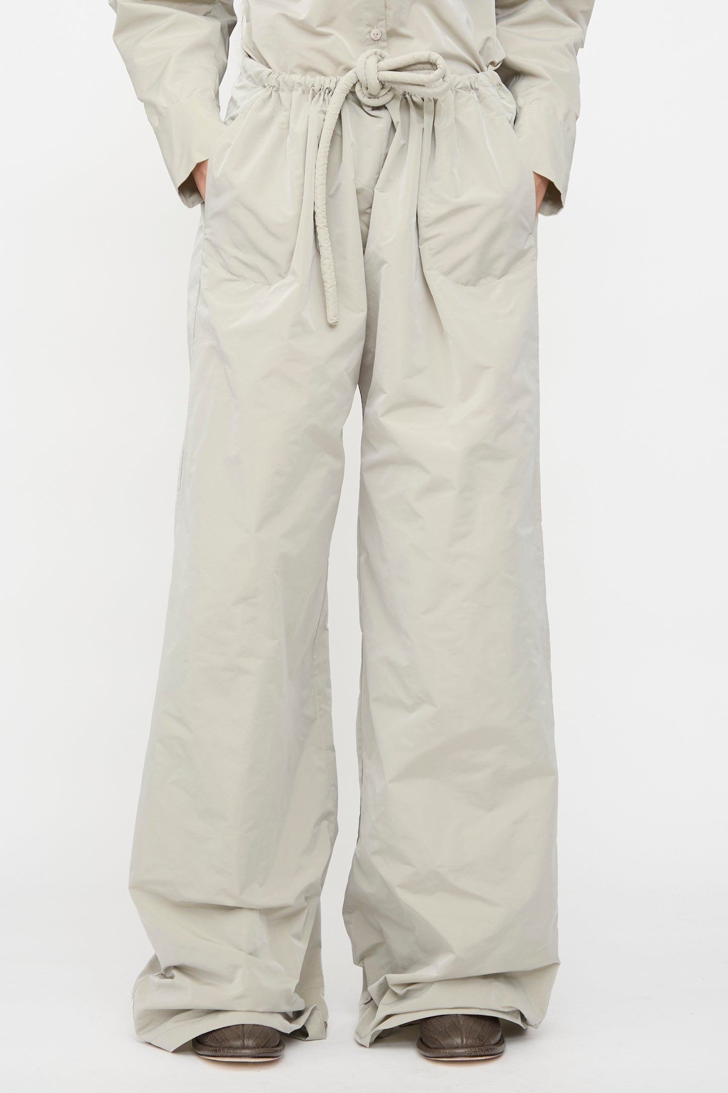 A person wearing Veronique Leroy's Tie Pants in Sage, featuring a high waist, wide legs, and drawstring waist, with hands in pockets, stands against a plain white background.