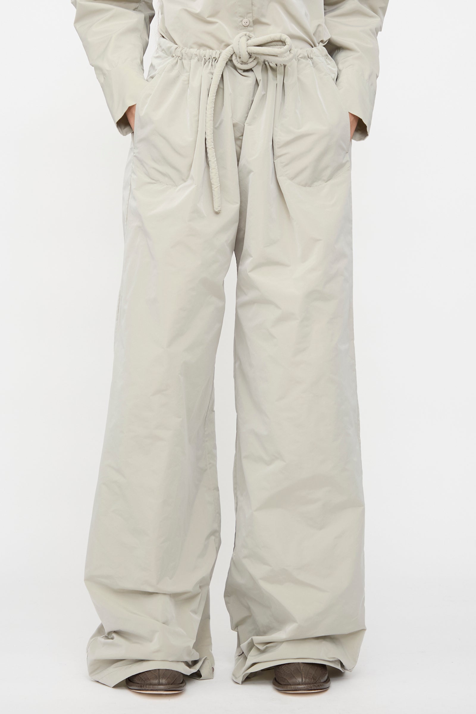 A person wearing Veronique Leroy's Tie Pants in Sage, featuring a high waist, wide legs, and drawstring waist, with hands in pockets, stands against a plain white background.