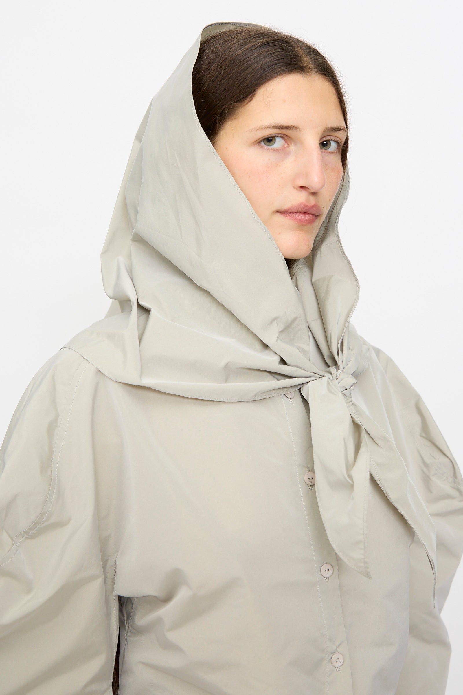 A woman wears the Veronique Leroy Top with Scarf in Sage, featuring balloon sleeves and a matching hooded scarf tied under her chin, as she looks at the camera against a plain background.