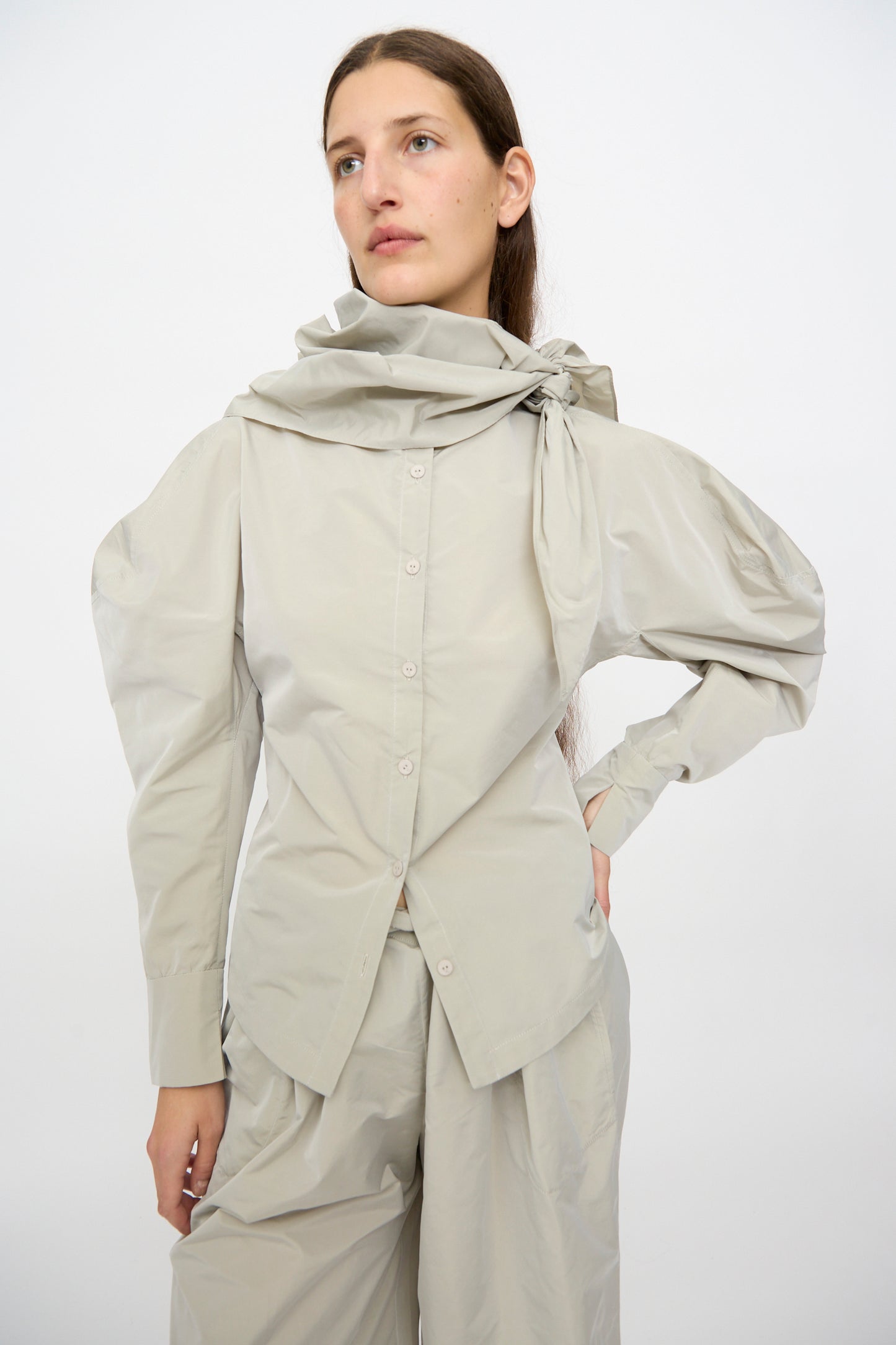 A person wearing the Veronique Leroy Top with Scarf in Sage, featuring a unique draped collar, paired with matching wide-leg pants, stands against a plain white background.