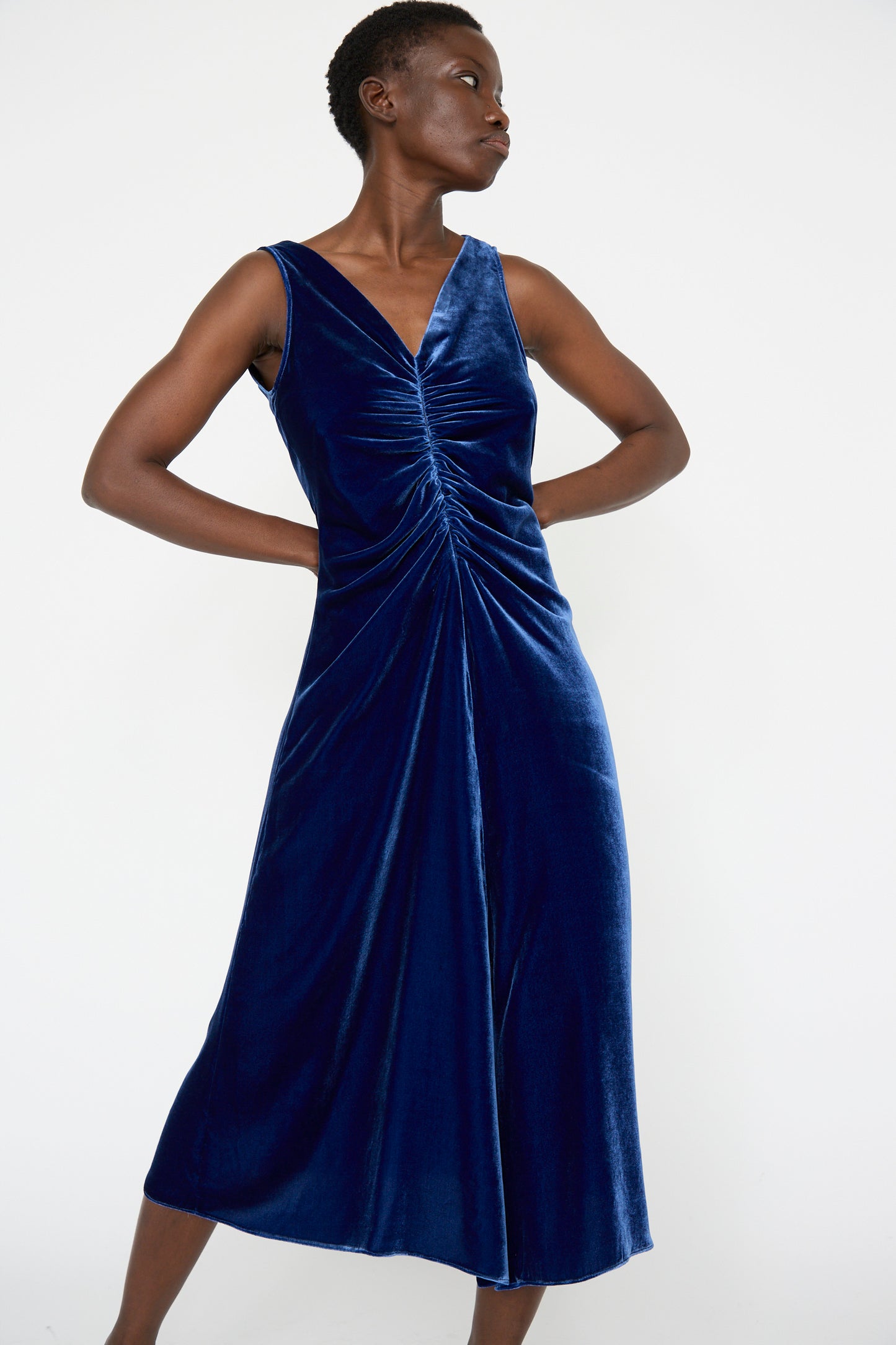 A woman wearing the Velvet Gather Front Dress in Cobalt by Veronique Leroy, features v-neckline and ruched front detail, while standing against a plain background.