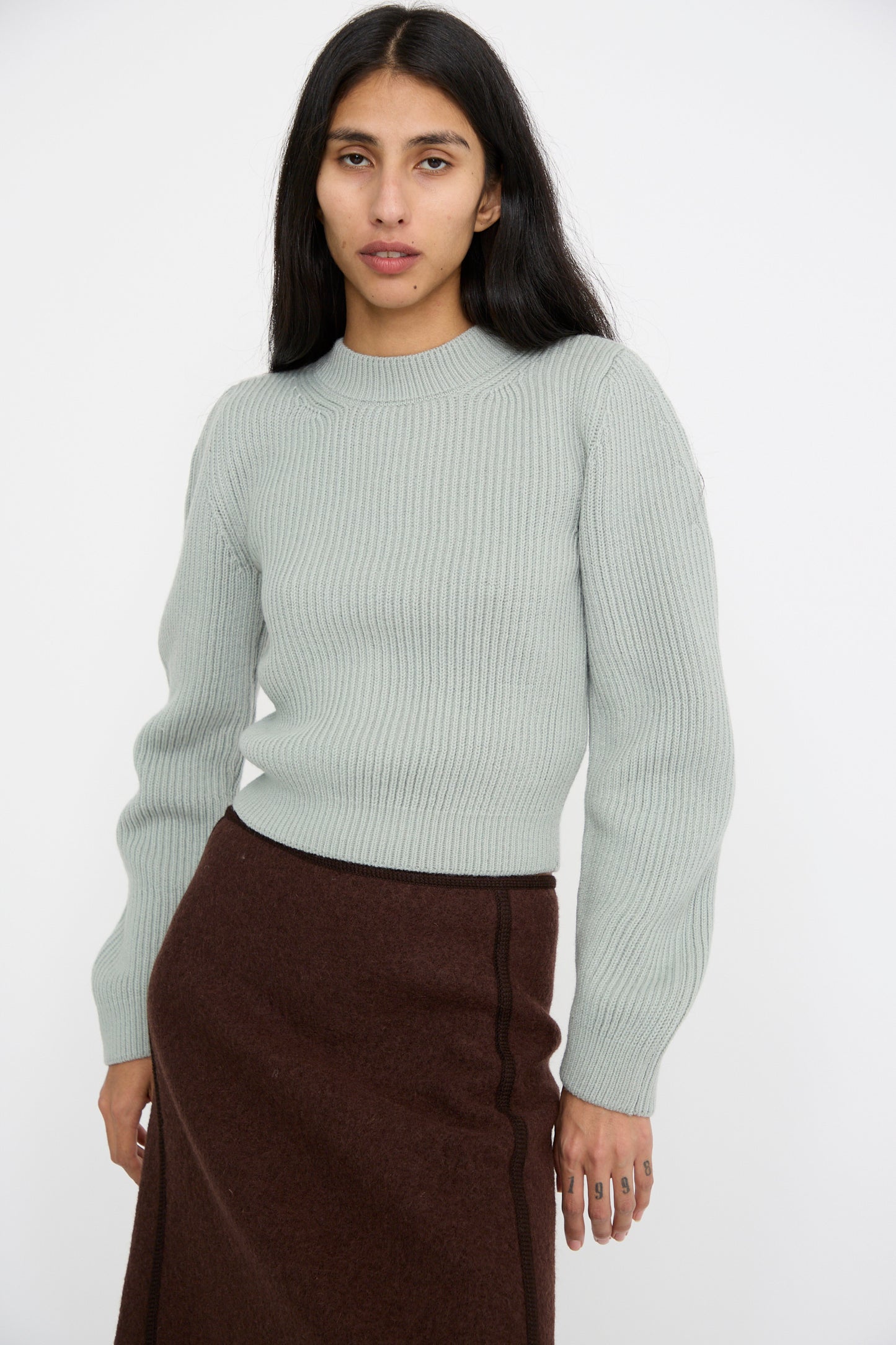 A person wearing the Veronique Leroy Wavy Sleeve Sweater in Fog paired with a brown skirt stands against a white background facing forward.