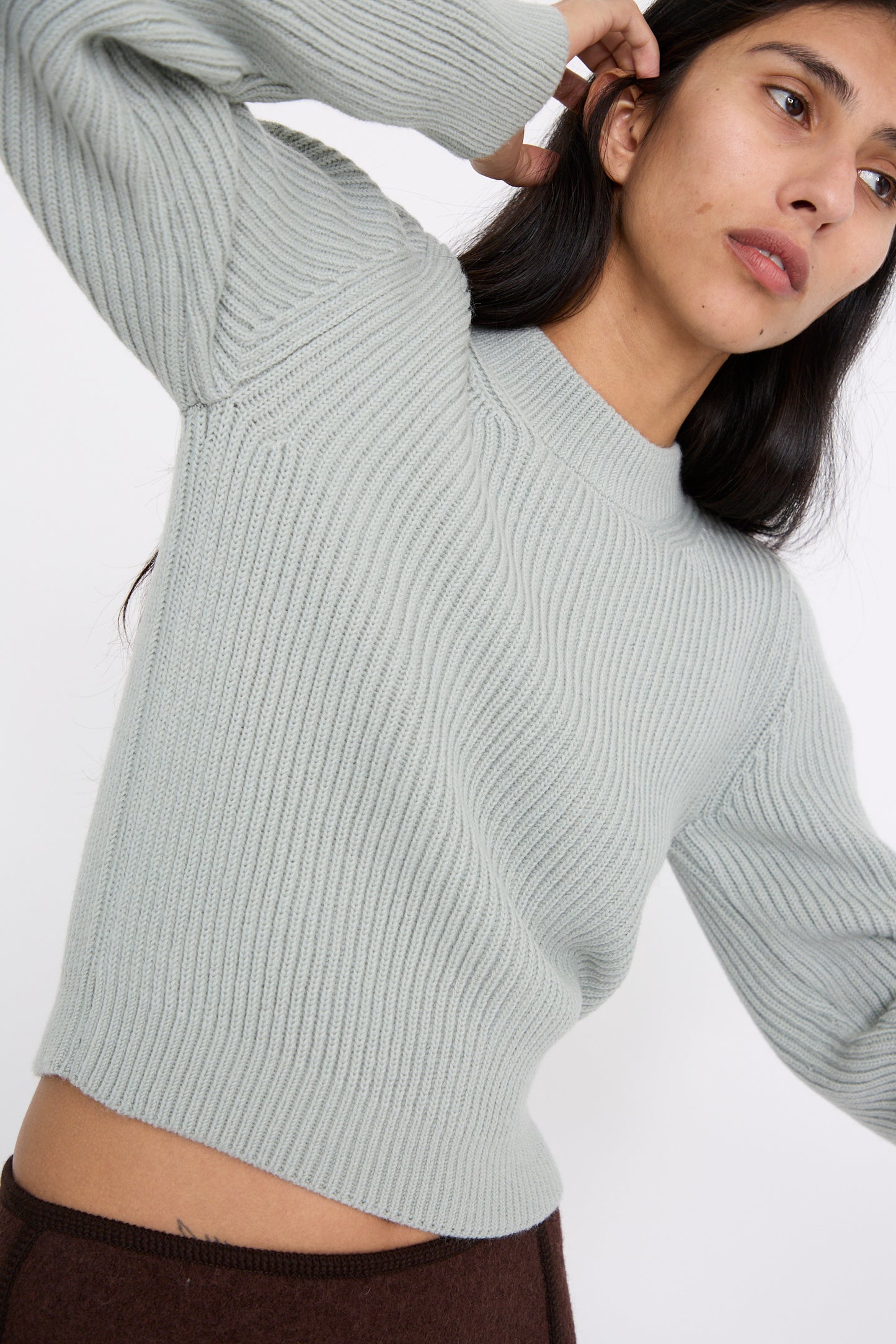 A person raising one arm while wearing the Wavy Sleeve Sweater in Fog by Veronique Leroy, crafted from Italian wool.