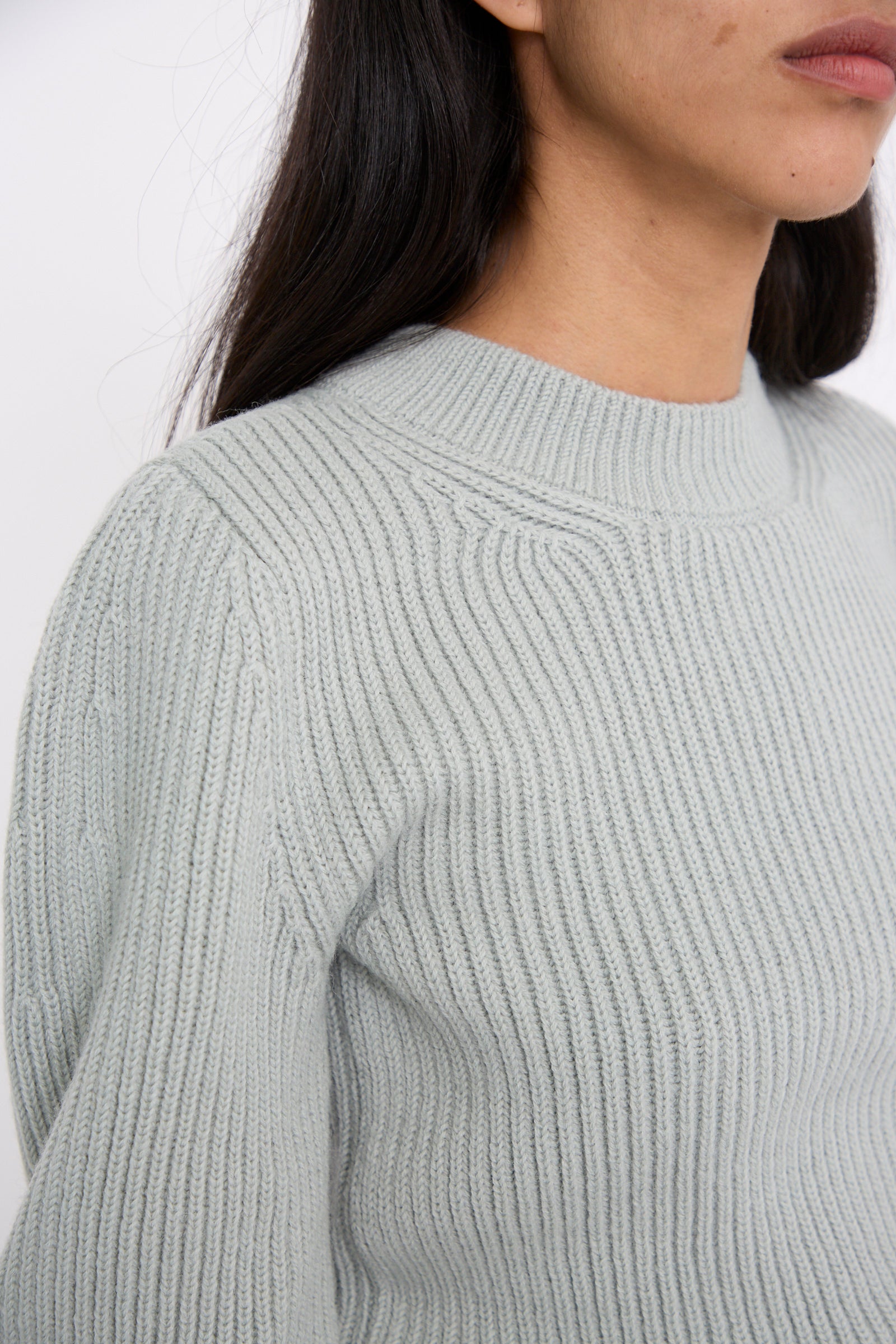 Close-up of a person wearing the Wavy Sleeve Sweater in Fog by Veronique Leroy. The image captures the upper torso and shoulder area, emphasizing the elegant wavy sleeves and long dark hair.