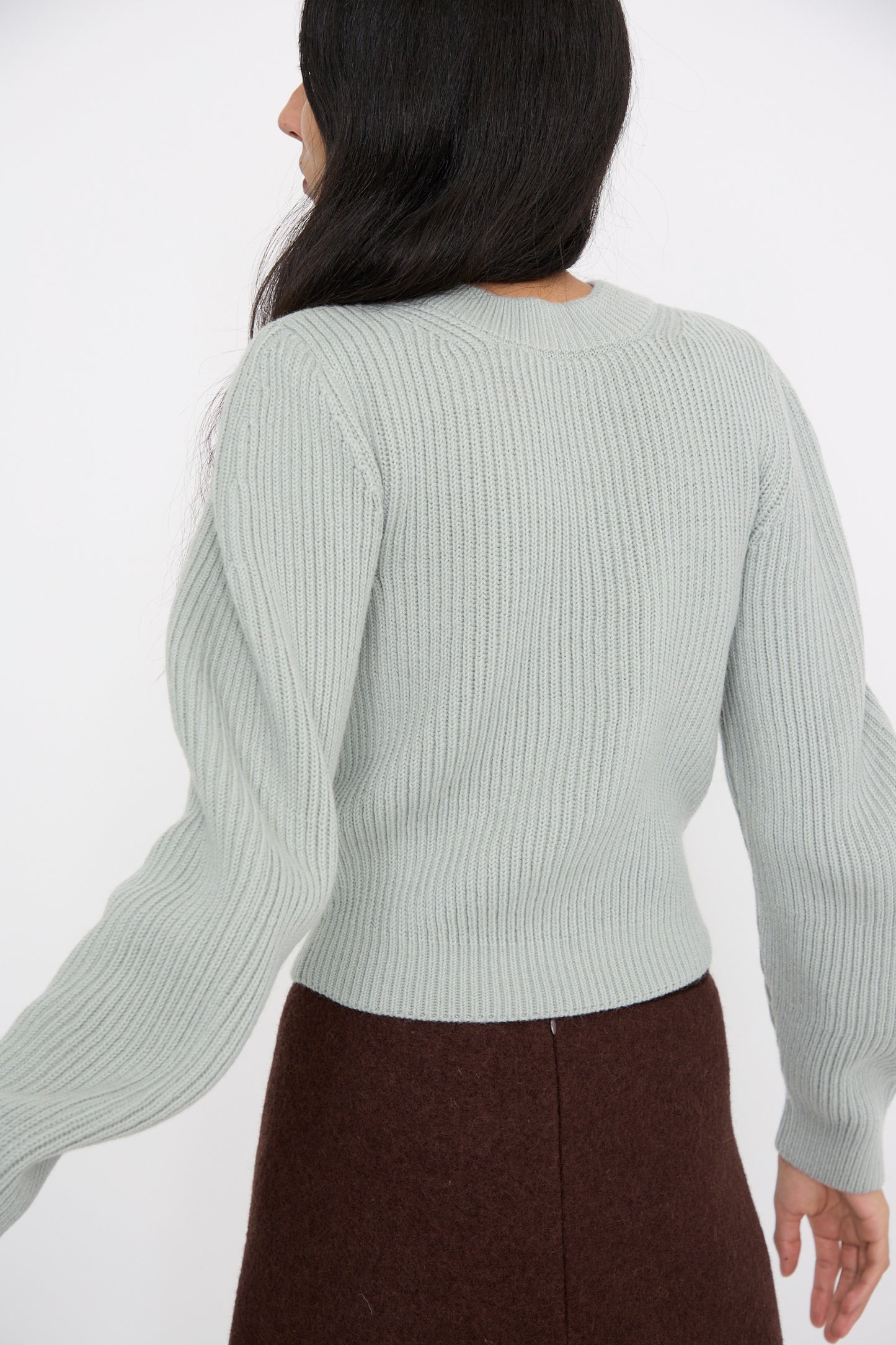 Person with long dark hair, wearing the Wavy Sleeve Sweater in Fog by Veronique Leroy paired with a brown skirt, facing away.