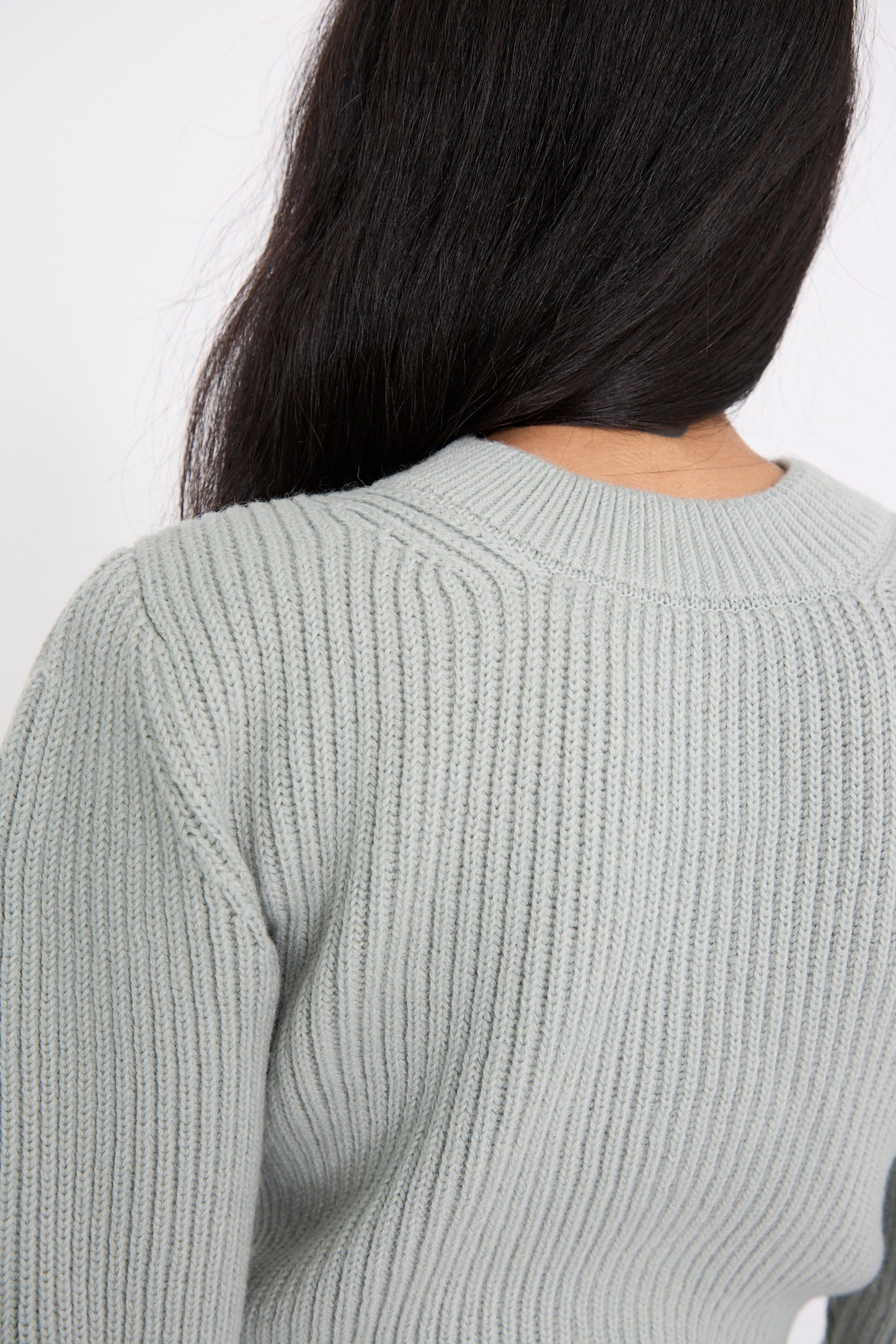 A person with long dark hair is seen from the back wearing the Veronique Leroy Wavy Sleeve Sweater in Fog.