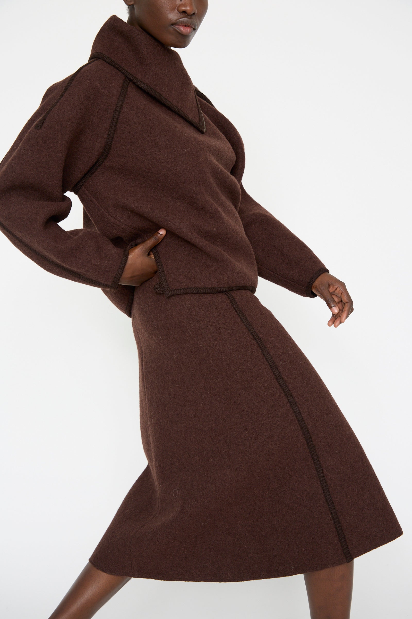 A person is wearing a brown ensemble, featuring a virgin wool top with a wide collar and the Wool Long Skirt in Choco by Veronique Leroy, standing against a plain white background.