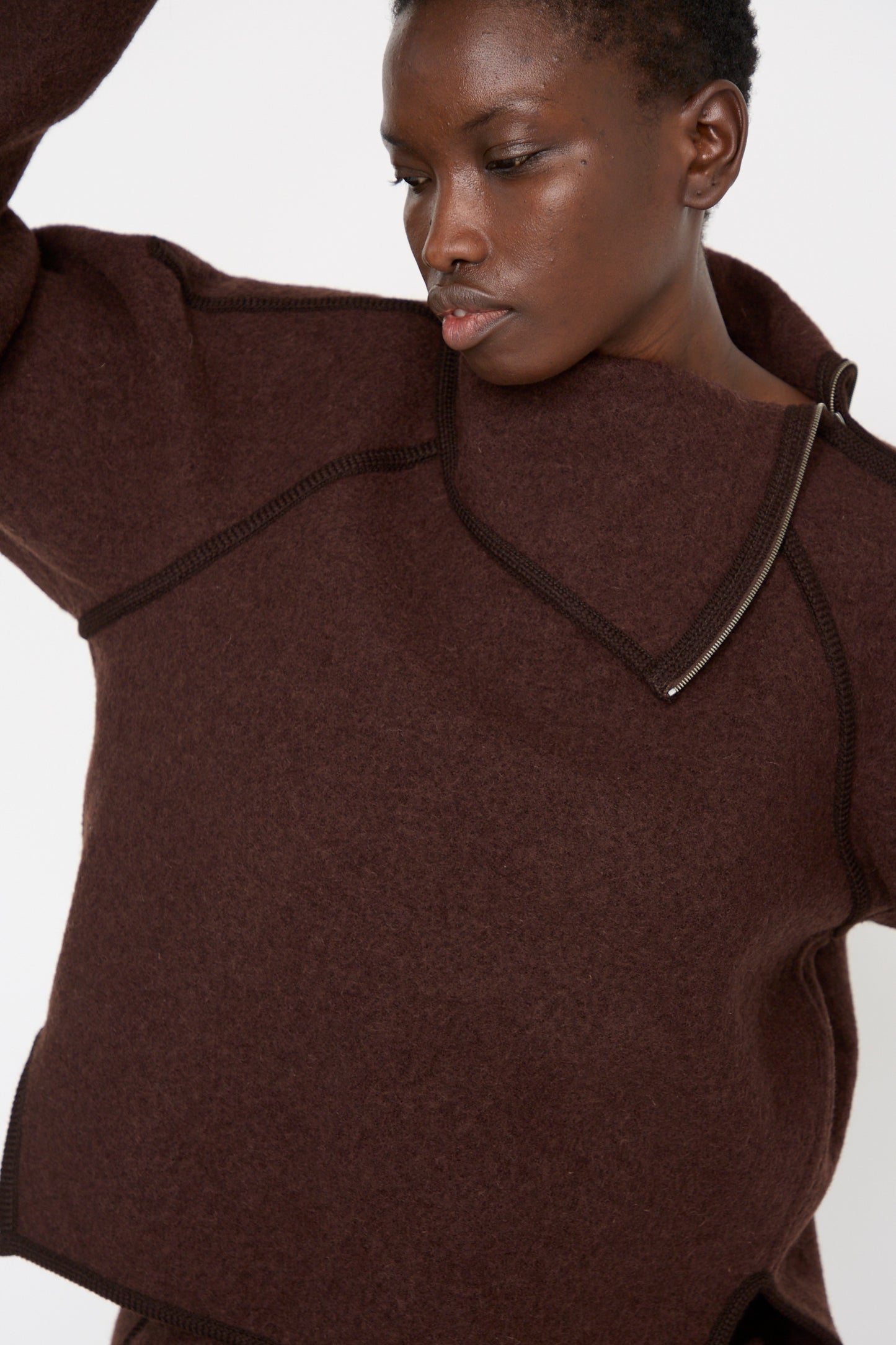 A person wearing the Wool Zip Neck Sweater in Choco by Veronique Leroy, featuring a textured dark brown design crafted from luxurious virgin wool and an oversized high collar.