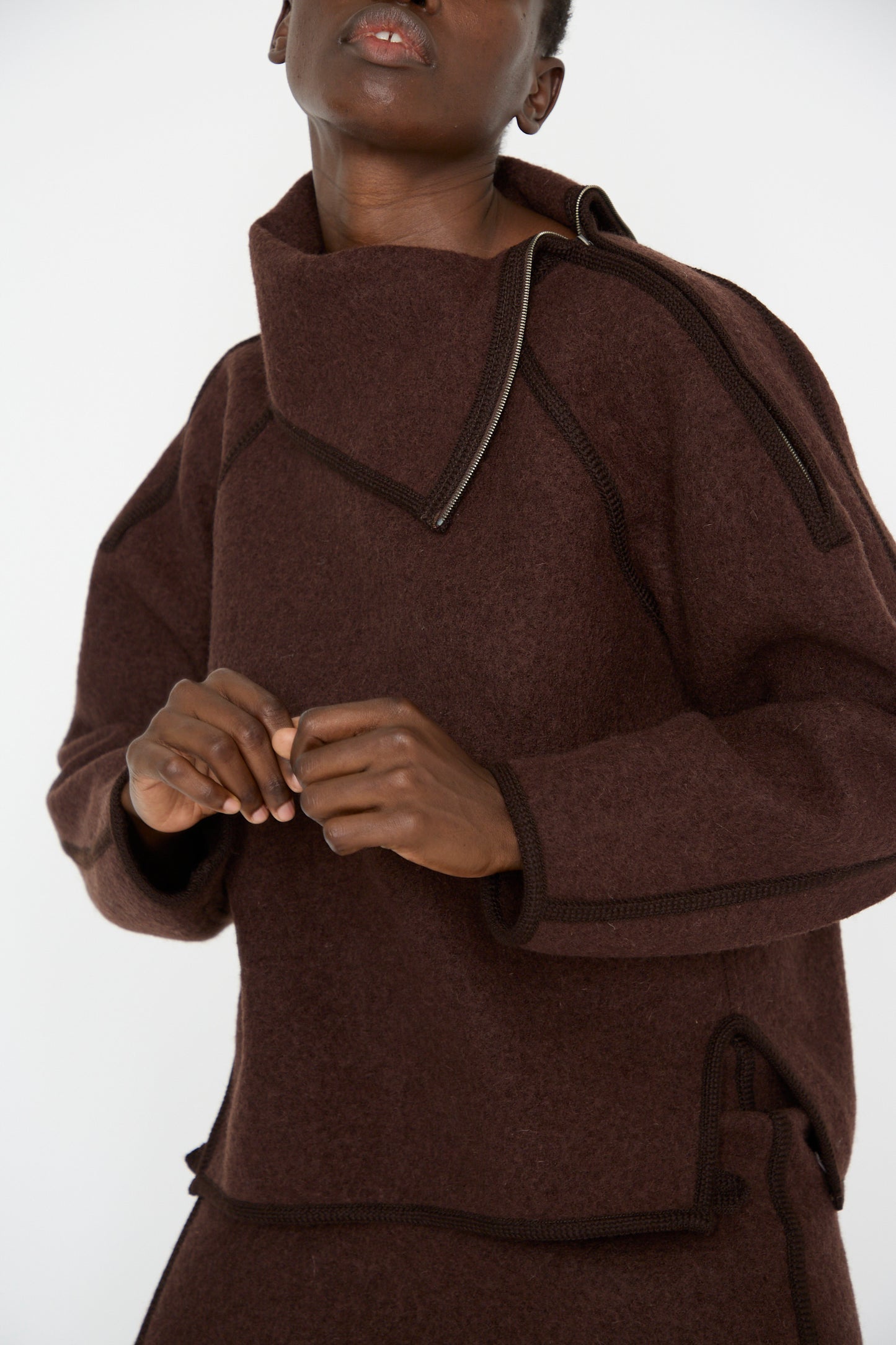 A person stands against a plain background wearing the Wool Zip Neck Sweater in Choco from Veronique Leroy, featuring an oversized design crafted from luxurious Italian boiled wool with unique seam detailing and a high collar.