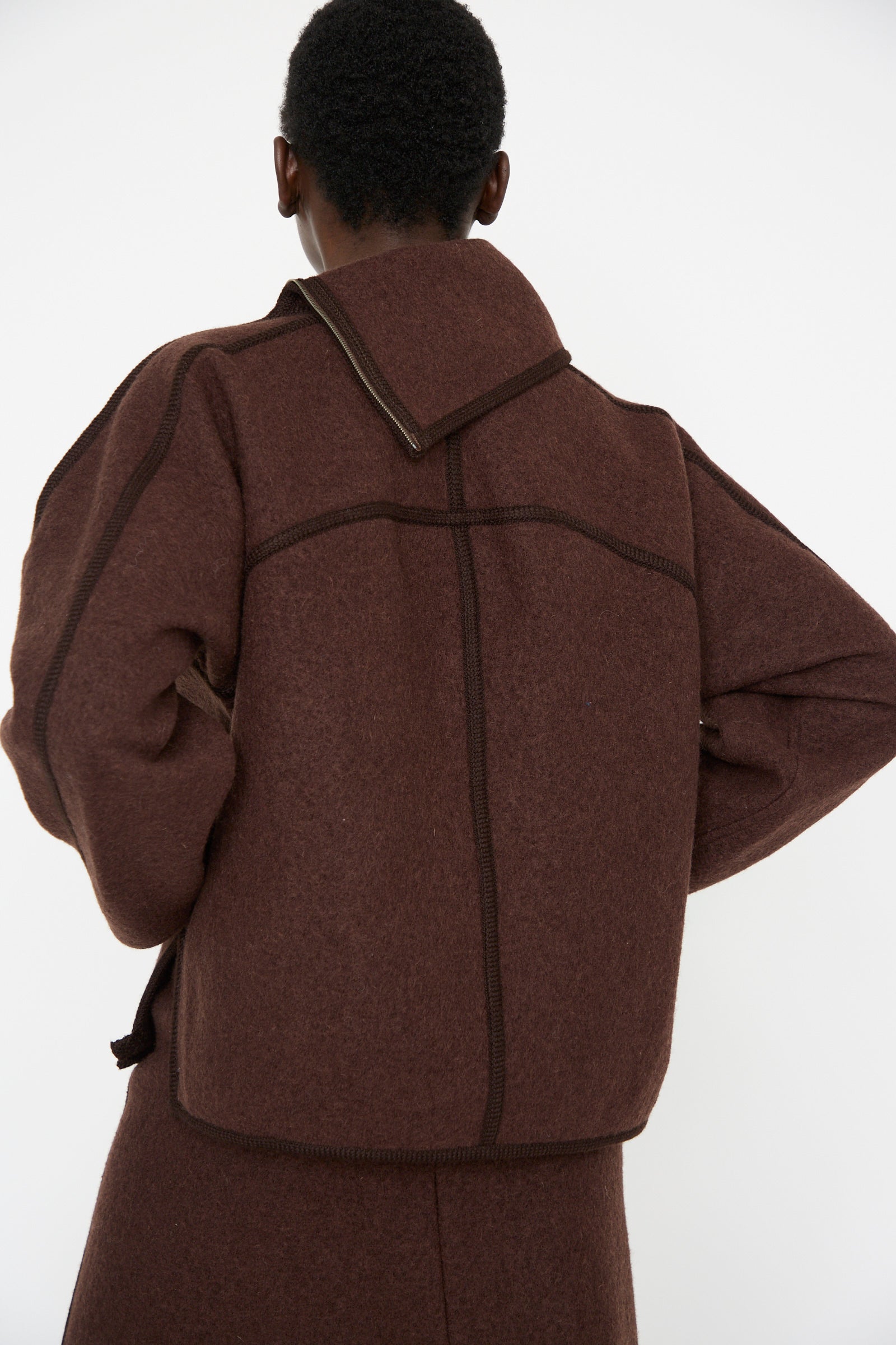 A person is seen from behind against a plain background, wearing the Wool Zip Neck Sweater in Choco by Veronique Leroy.