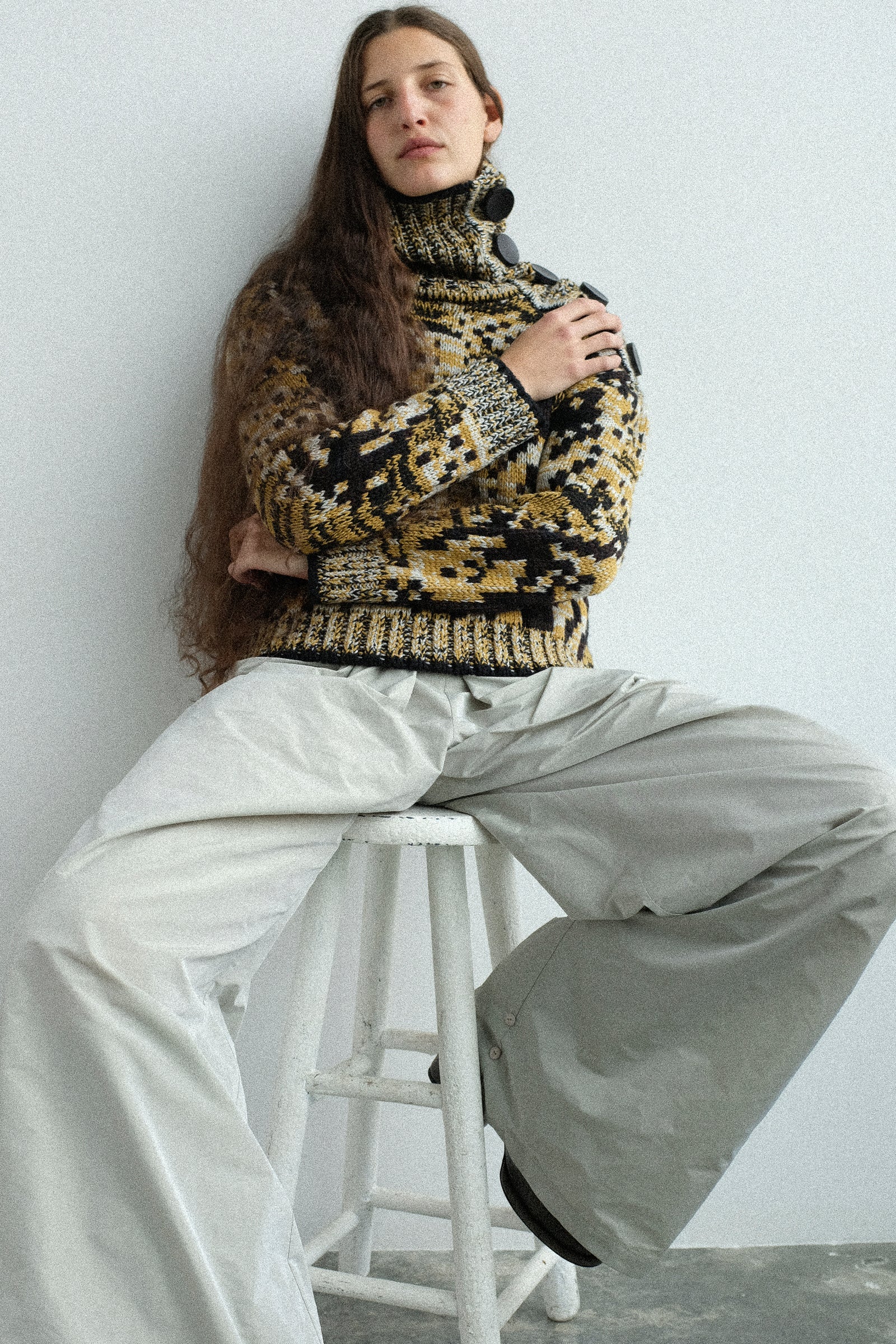 Person wearing pieces from the Veronique Leroy FW25 collection, sitting on a stool against a white wall.
