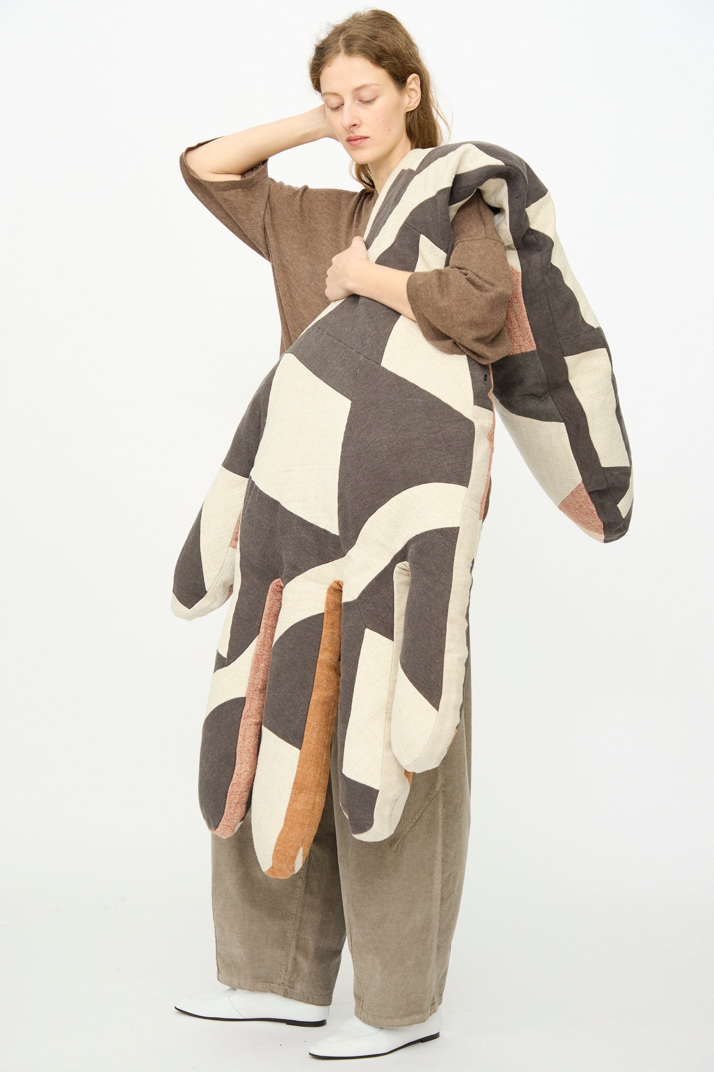 A woman holds the Sonia Delaunay Tissu Simultané Giant Hand Bolster I by Wiener Times, a large hand-shaped pillow, against a plain background.