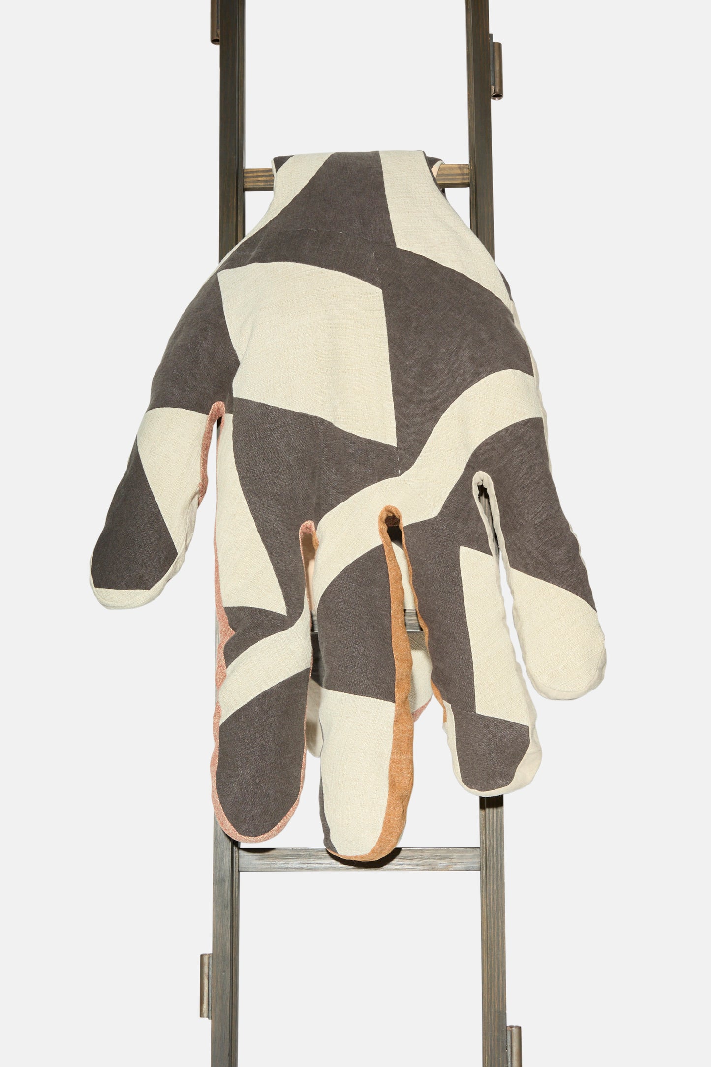 The Sonia Delaunay Tissu Simultané Giant Hand Bolster I by Wiener Times, featuring bold black, white, and beige geometric patterns, is draped over a metal ladder against a plain white background.