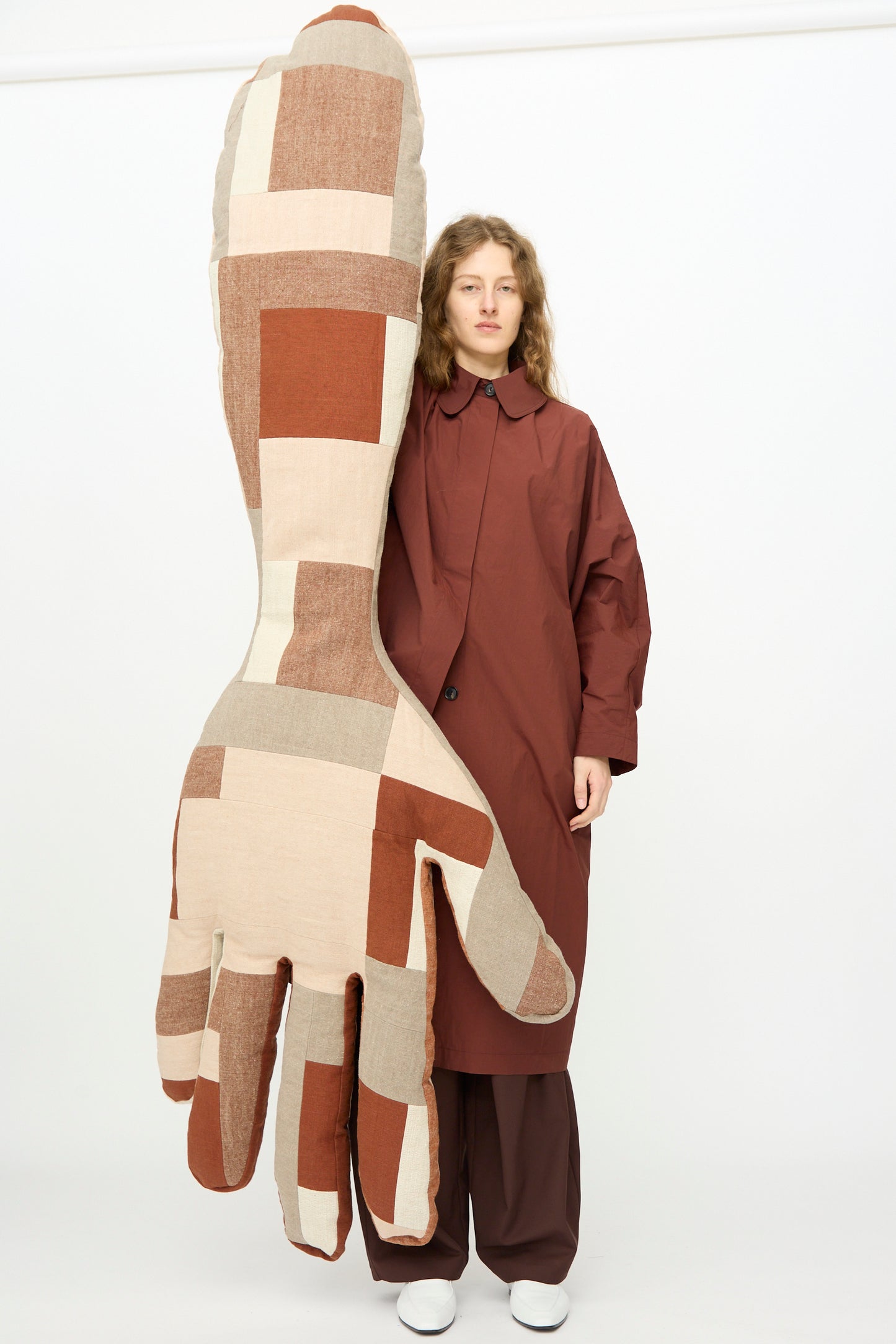A person in loose brown clothing stands against a white background, holding the Sonia Delaunay Tissu Simultané Giant Hand Bolster II by Wiener Times.