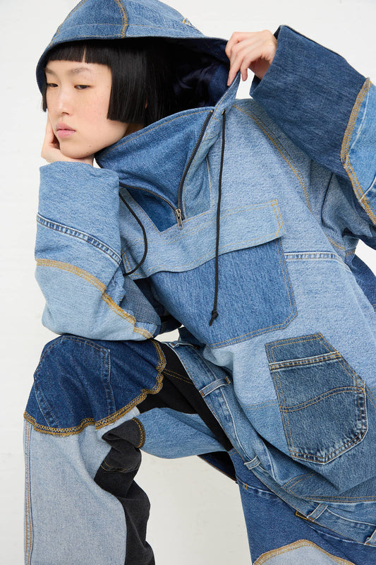 A person wearing an Anorak in Blue by WildRootz, a hooded, patchwork denim outfit made from recycled denim, is sitting and resting their face on their hand.