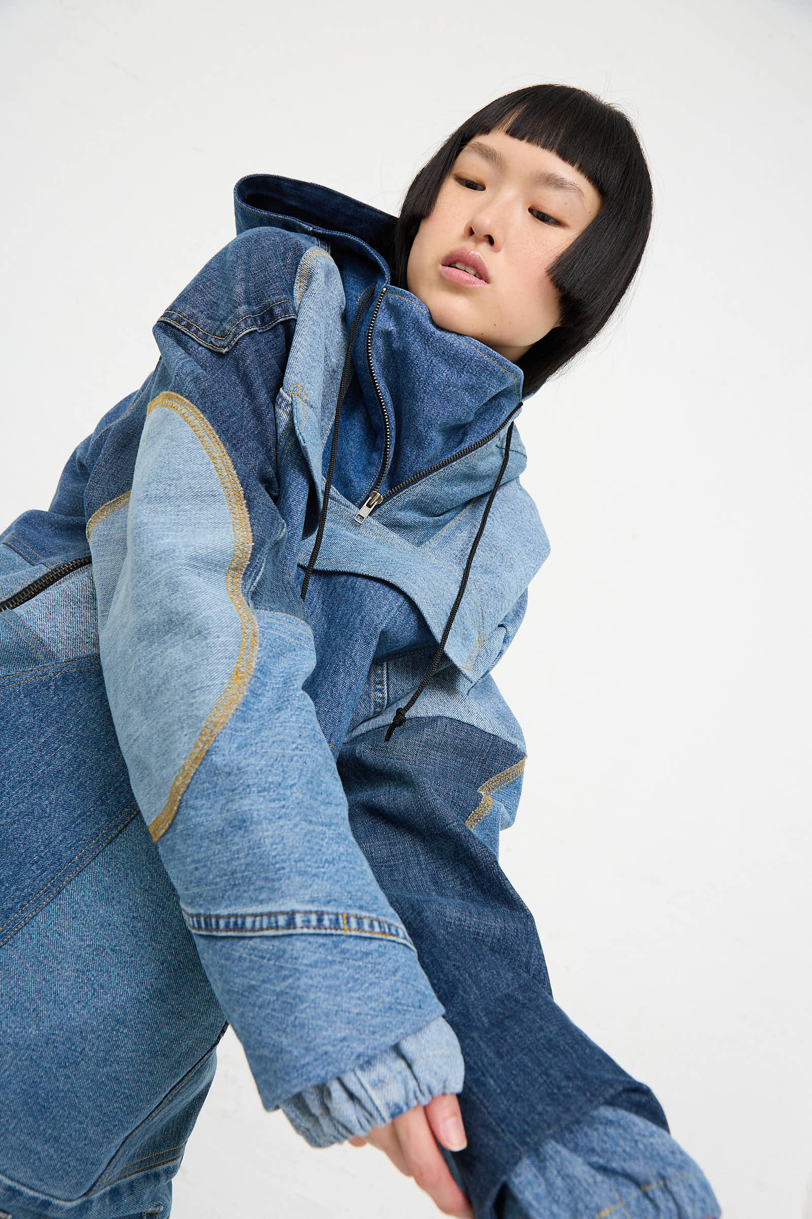 A person with short black hair is looking down, wearing a patched, handmade denim "Anorak in Blue" jacket from WildRootz.