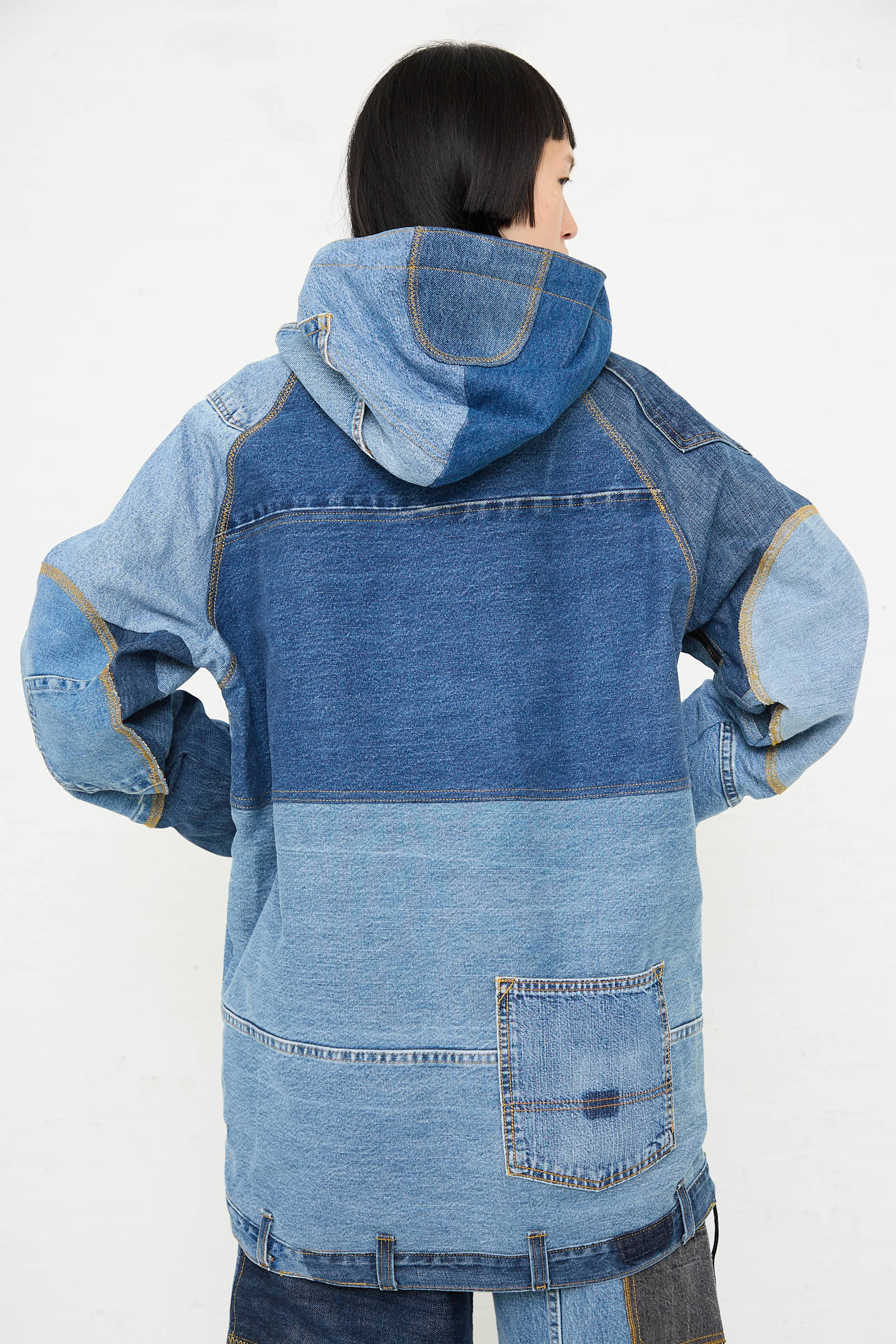 Person wearing a WildRootz Anorak in Blue, a handmade patchwork-style denim jacket with a hood, crafted from recycled denim, viewed from behind against a plain white background.