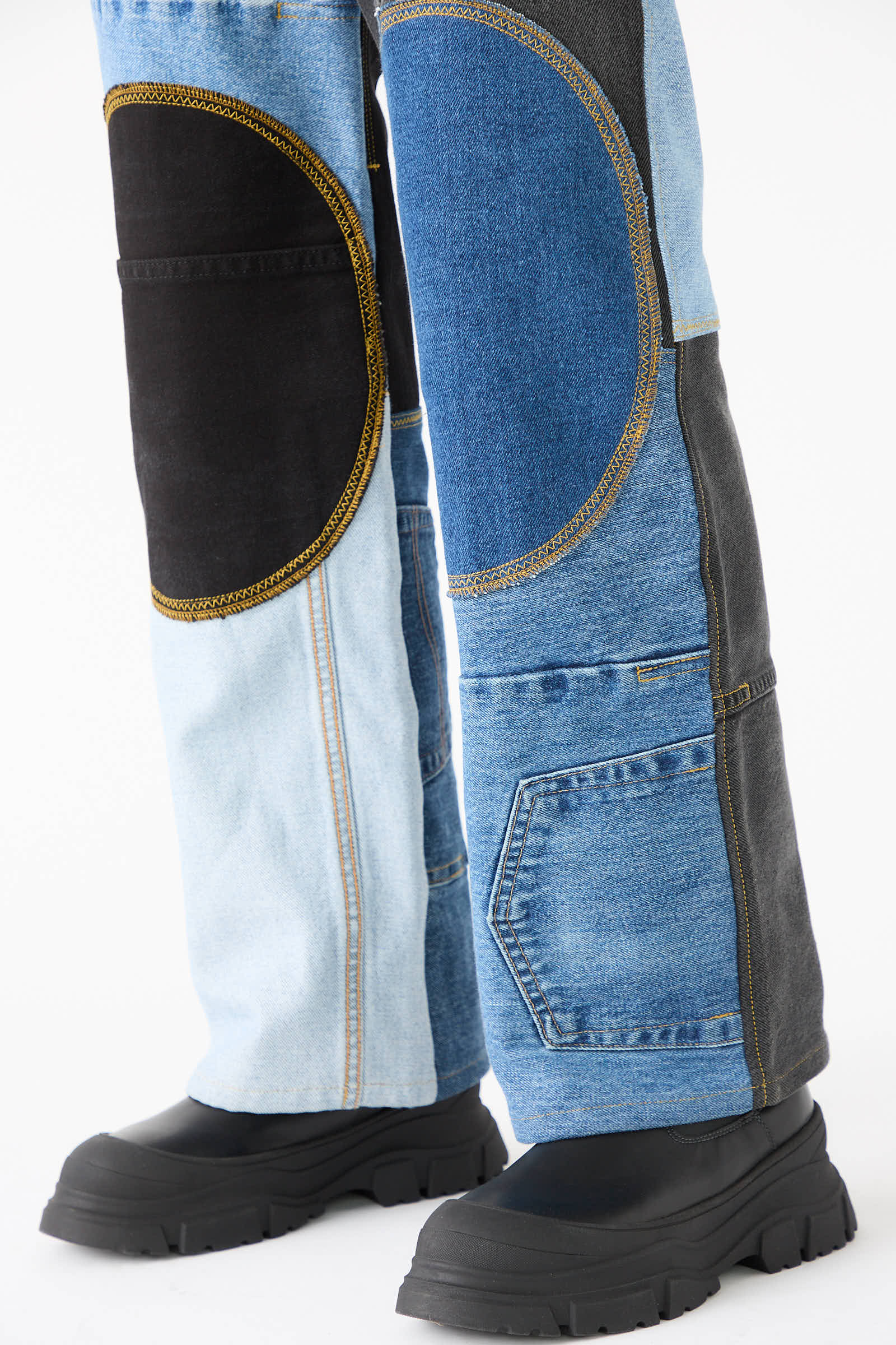 Person wearing WildRootz Reworked Jeans in blue, black, and grey shades, made from recycled denim, paired with black chunky boots, standing on a white background.