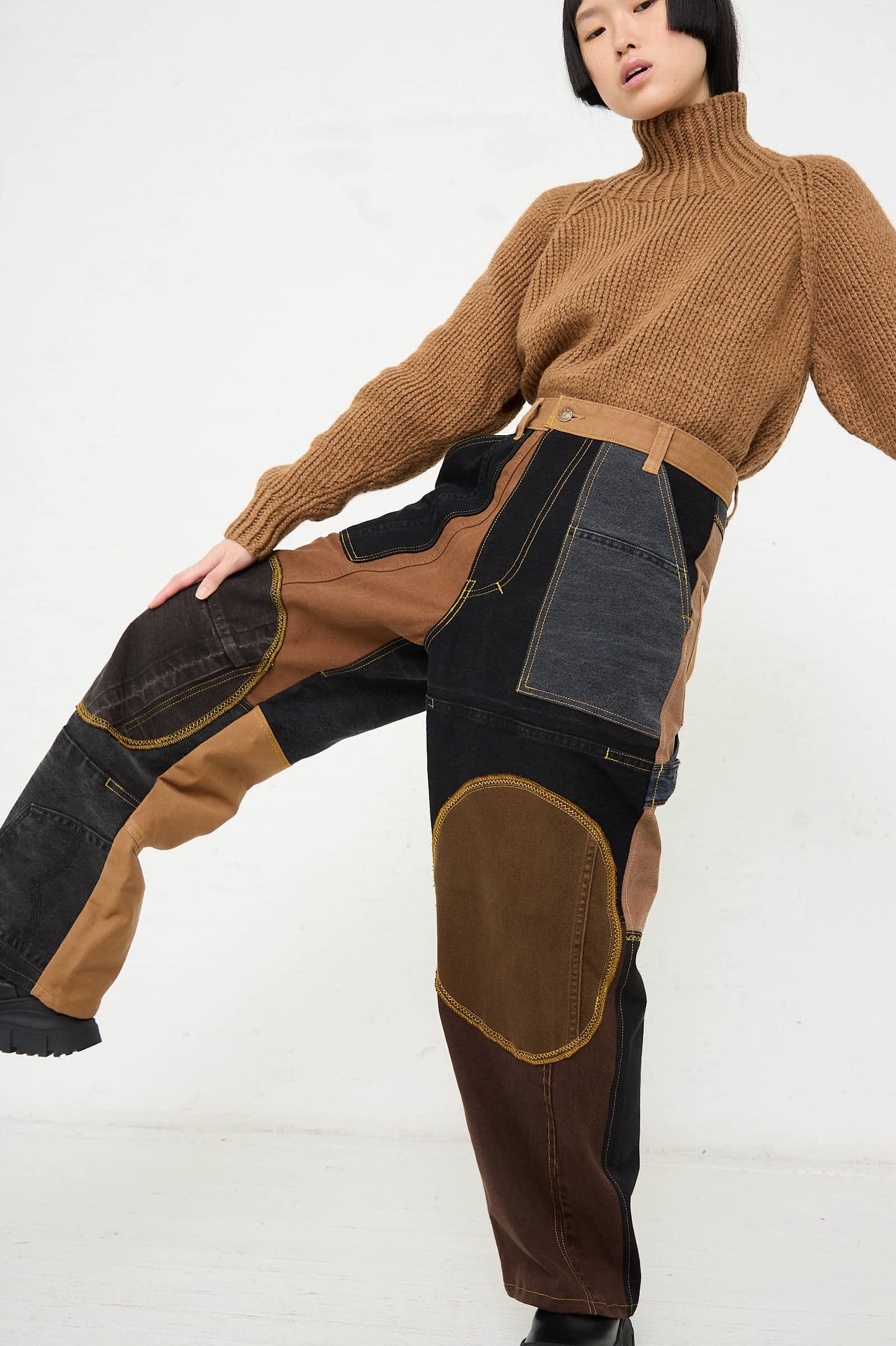 A person posing in a beige turtleneck sweater and WildRootz Reworked Jeans in Black and Brown I, handmade from recycled denim in New York, against a plain background.