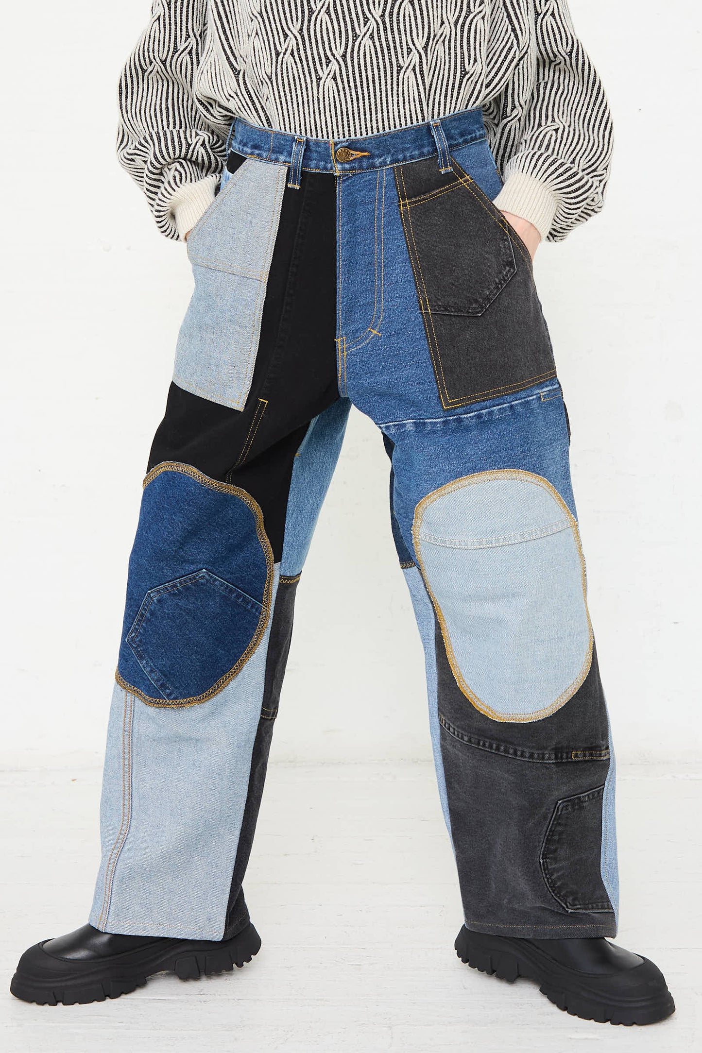 A person wearing Reworked Jeans in Blue, Black and Grey I by WildRootz along with a striped sweater, standing with their feet apart on a light-colored floor.