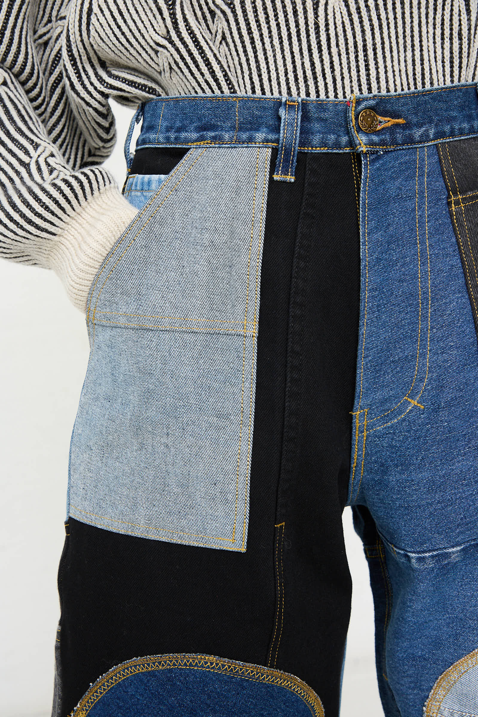 Close-up of a person wearing WildRootz Reworked Jeans in Blue, Black and Grey I made from recycled denim, paired with a black and white striped sweater. The person has one hand in a front pocket.