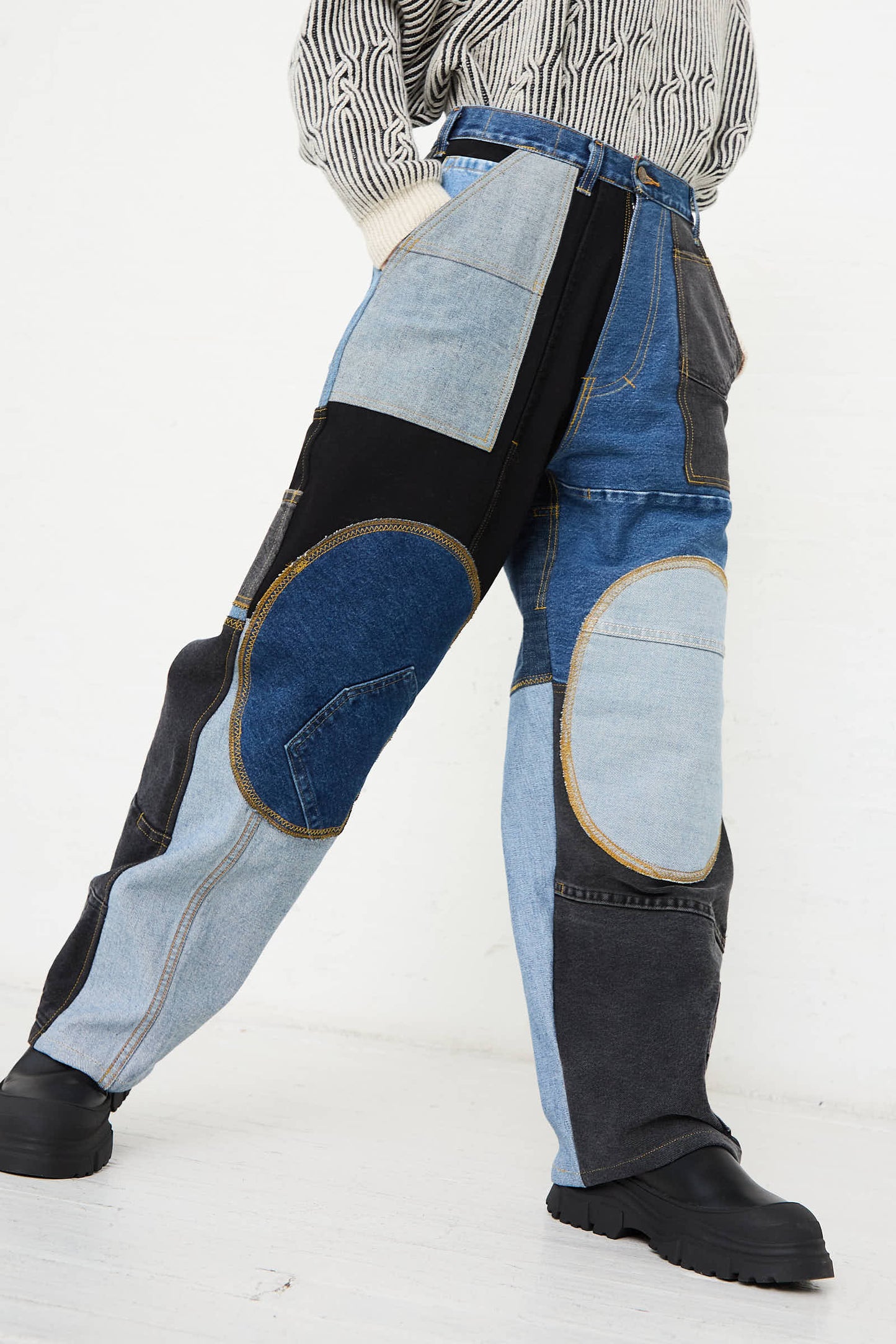 A person wears WildRootz Reworked Jeans in Blue, Black, and Grey I—handmade from recycled denim—and pairs them with black boots, standing against a plain white background.