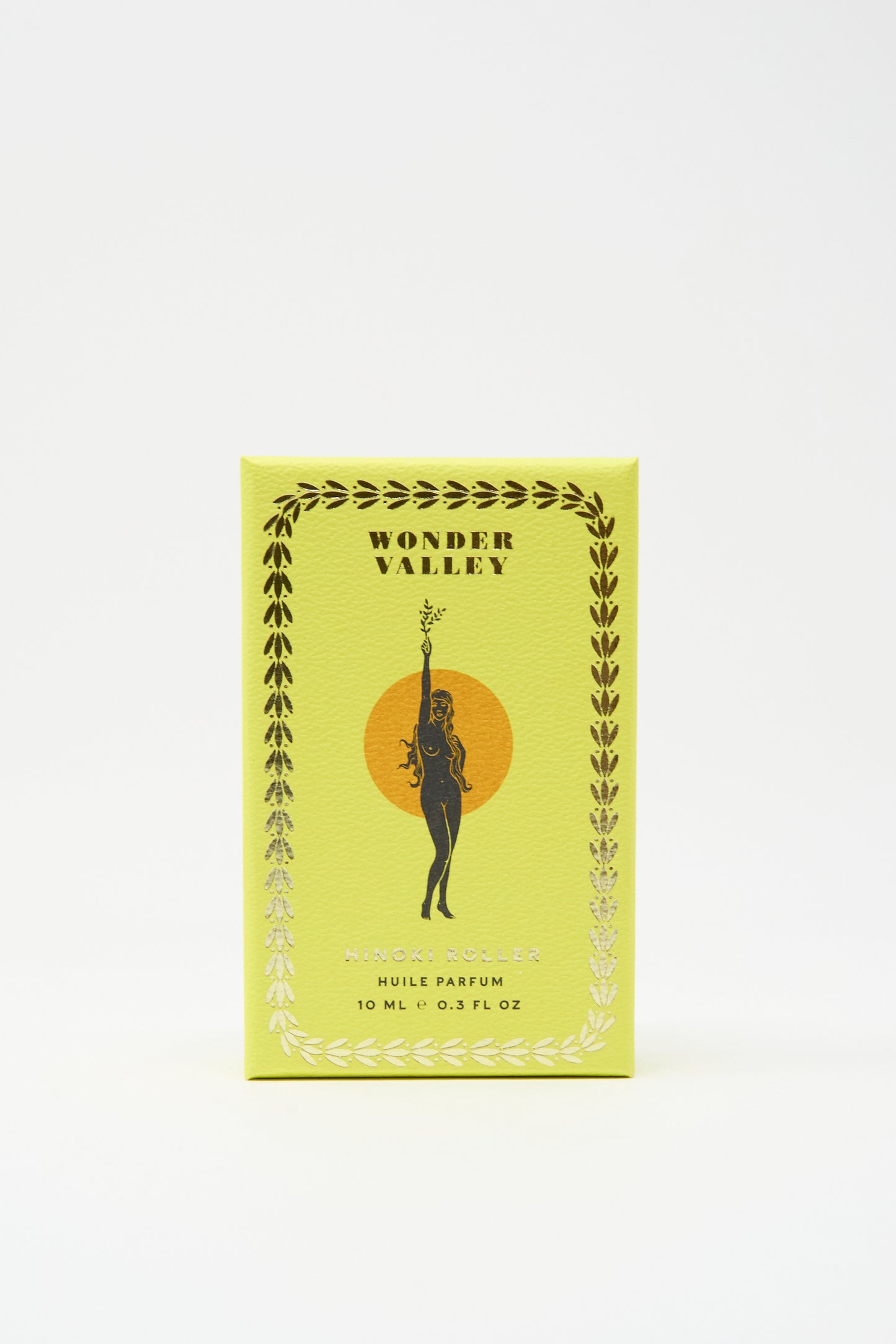 A yellow Wonder Valley box with a gold olive branch border showcases the black silhouette of a woman with a branch against an orange circle—perfect for gifting their Hinoki Roller essential oil-based perfume.