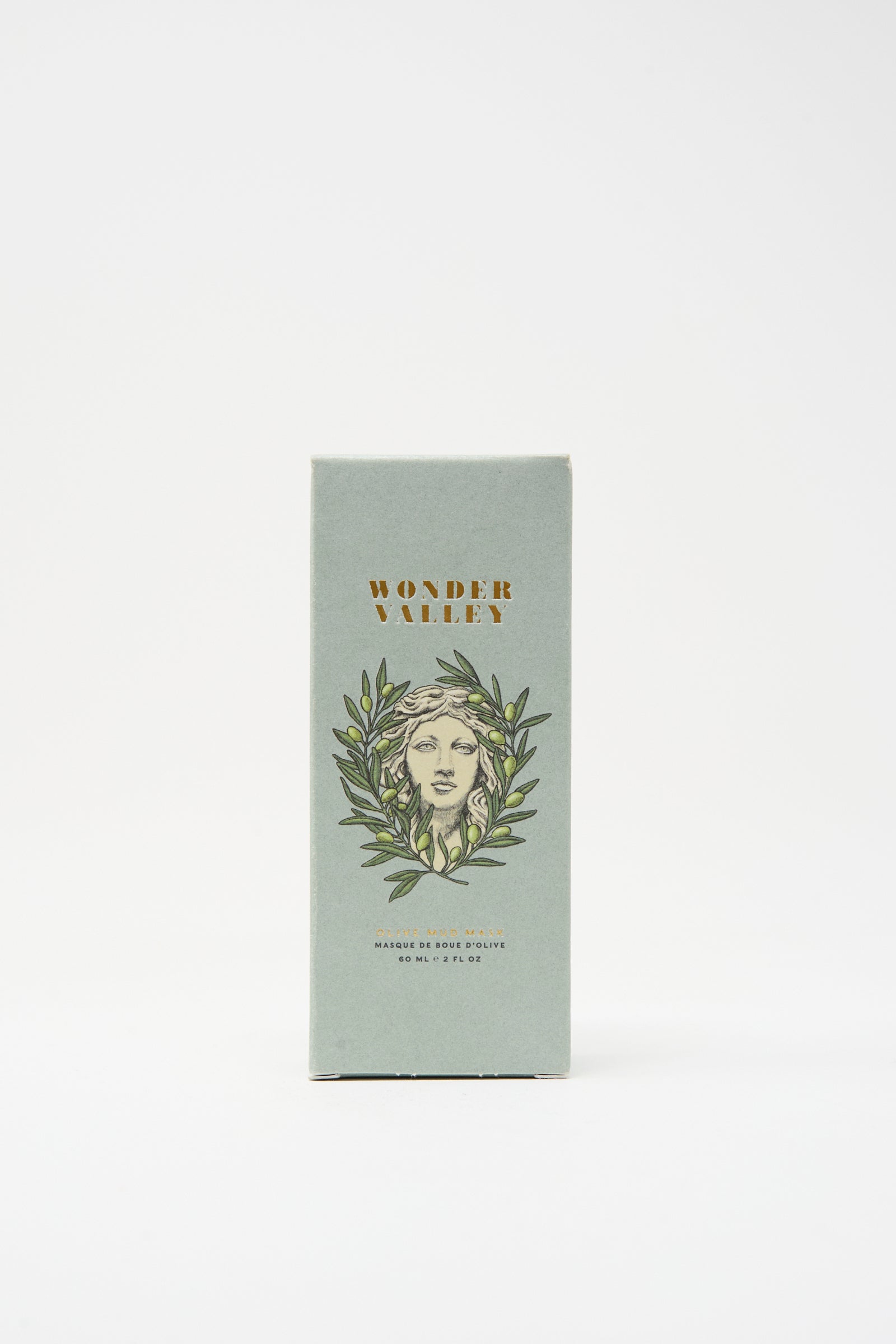 A rectangular box of Wonder Valley Olive Mud Mask, showing an illustrated face with olive branches on a light green background, stands upright on a white surface; hydrates and balances skin with an elegant touch.