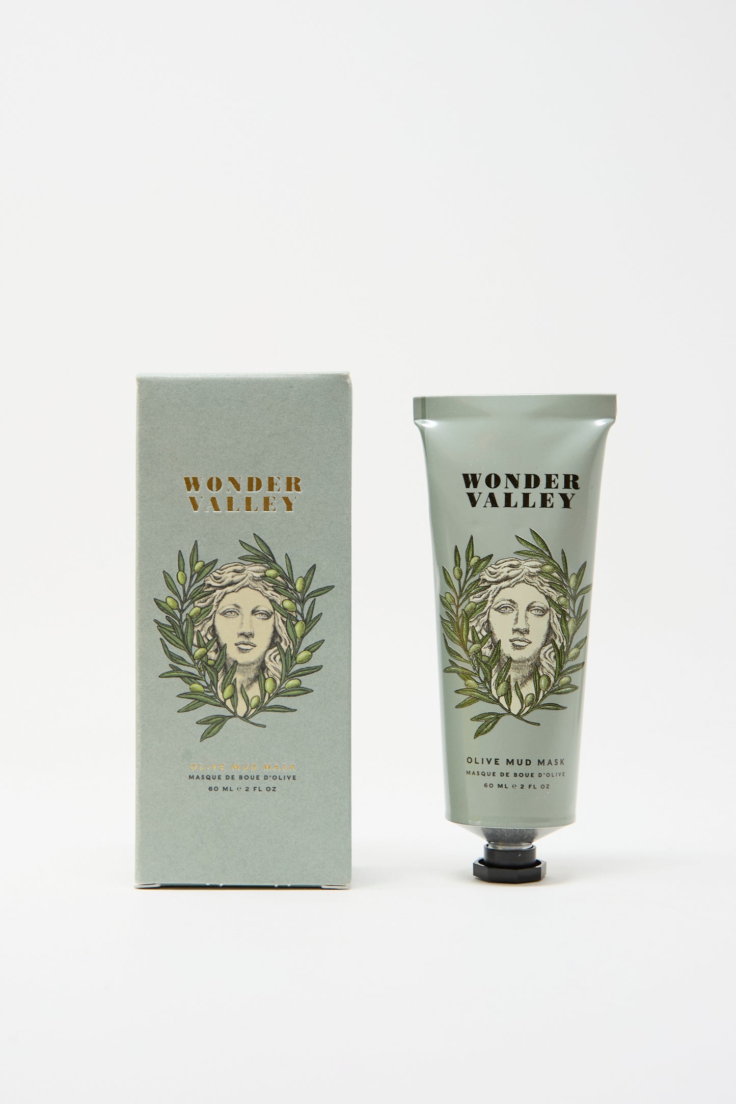 The Wonder Valley Olive Mud Mask is shown alongside its matching box, both featuring an illustrated face with olive branches on a light green background. This mask hydrates and balances skin for a refreshed look.
