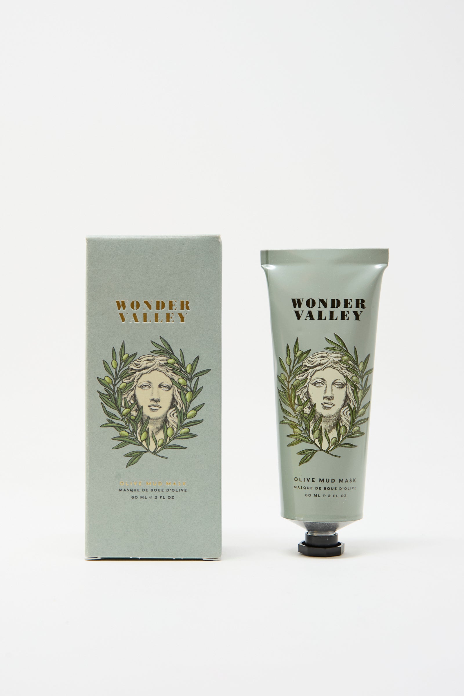 The Wonder Valley Olive Mud Mask is shown alongside its matching box, both featuring an illustrated face with olive branches on a light green background. This mask hydrates and balances skin for a refreshed look.