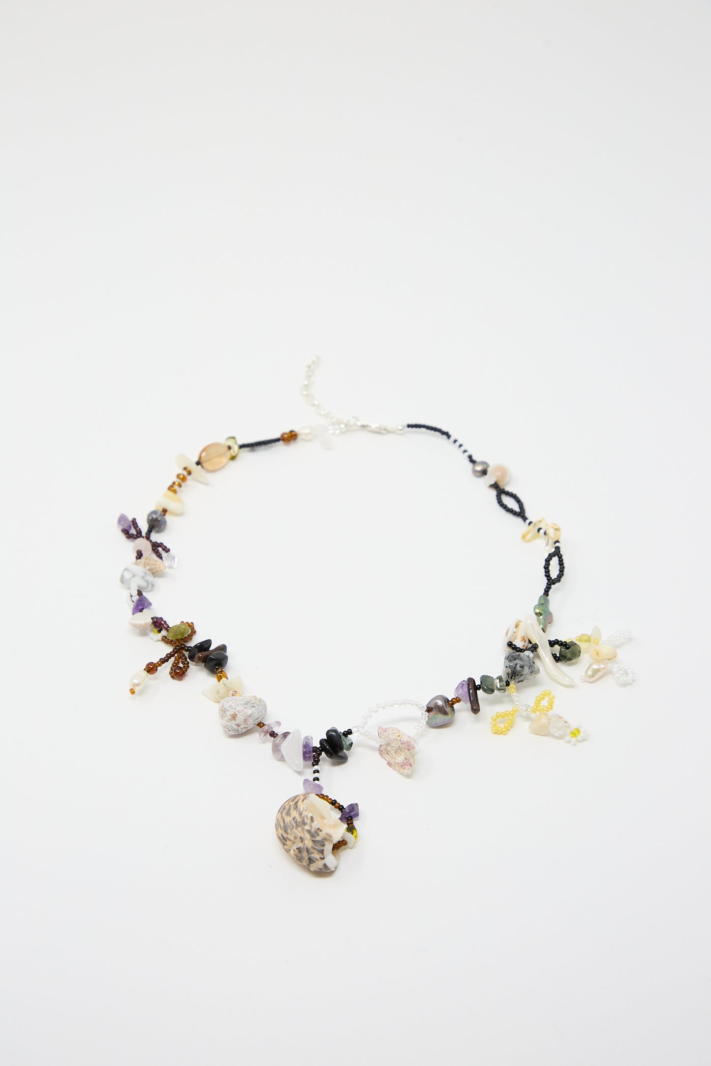 The "August is an Angel Necklace" by Yona Kohen is a stunning hand-beaded piece featuring multicolored gemstones, natural stones, and various glass beads, with a larger pendant in the center, displayed against a plain white background.