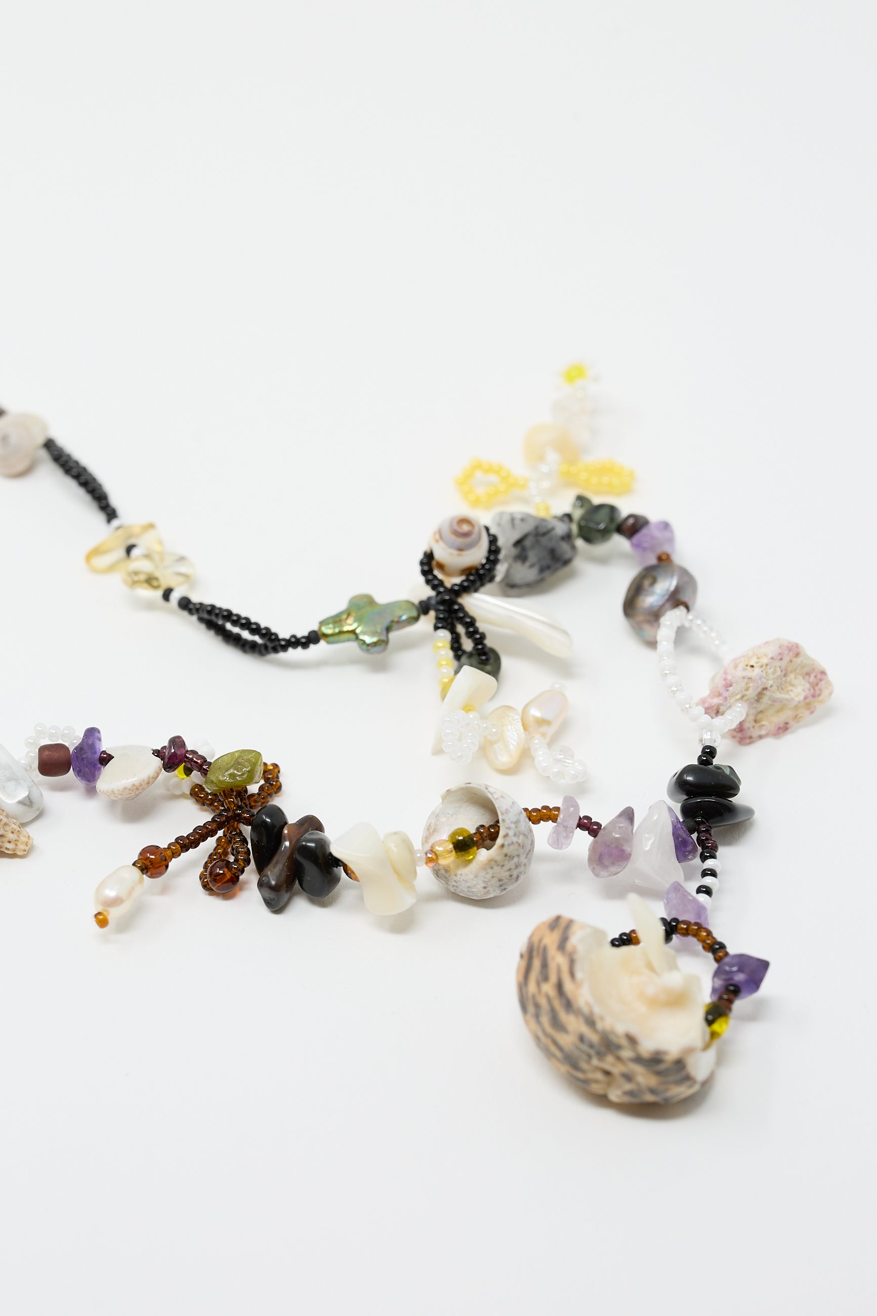 The "August is an Angel Necklace" by Yona Kohen, carefully crafted with a unique arrangement of various natural stones, shells, and small trinkets, is showcased on a white surface.