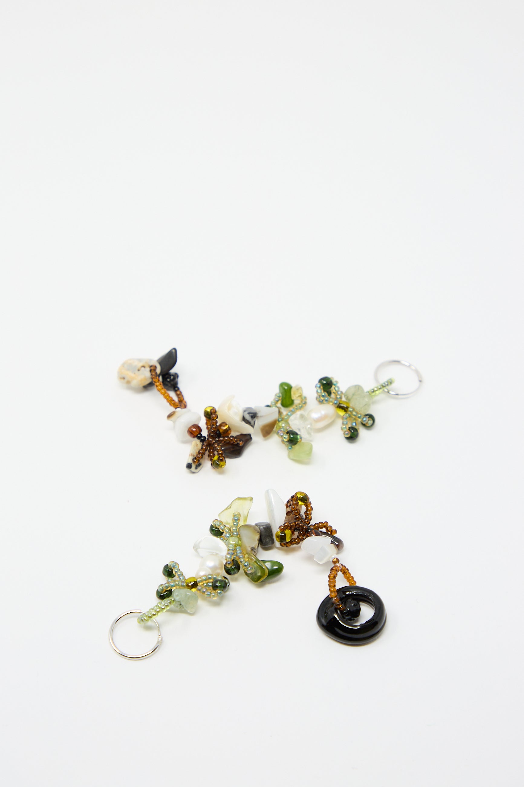 A set of Yona Kohen's Harvest Earrings 2.0, featuring an assortment of green, white, and brown glass beads along with small trinkets, artfully arranged on a white background.