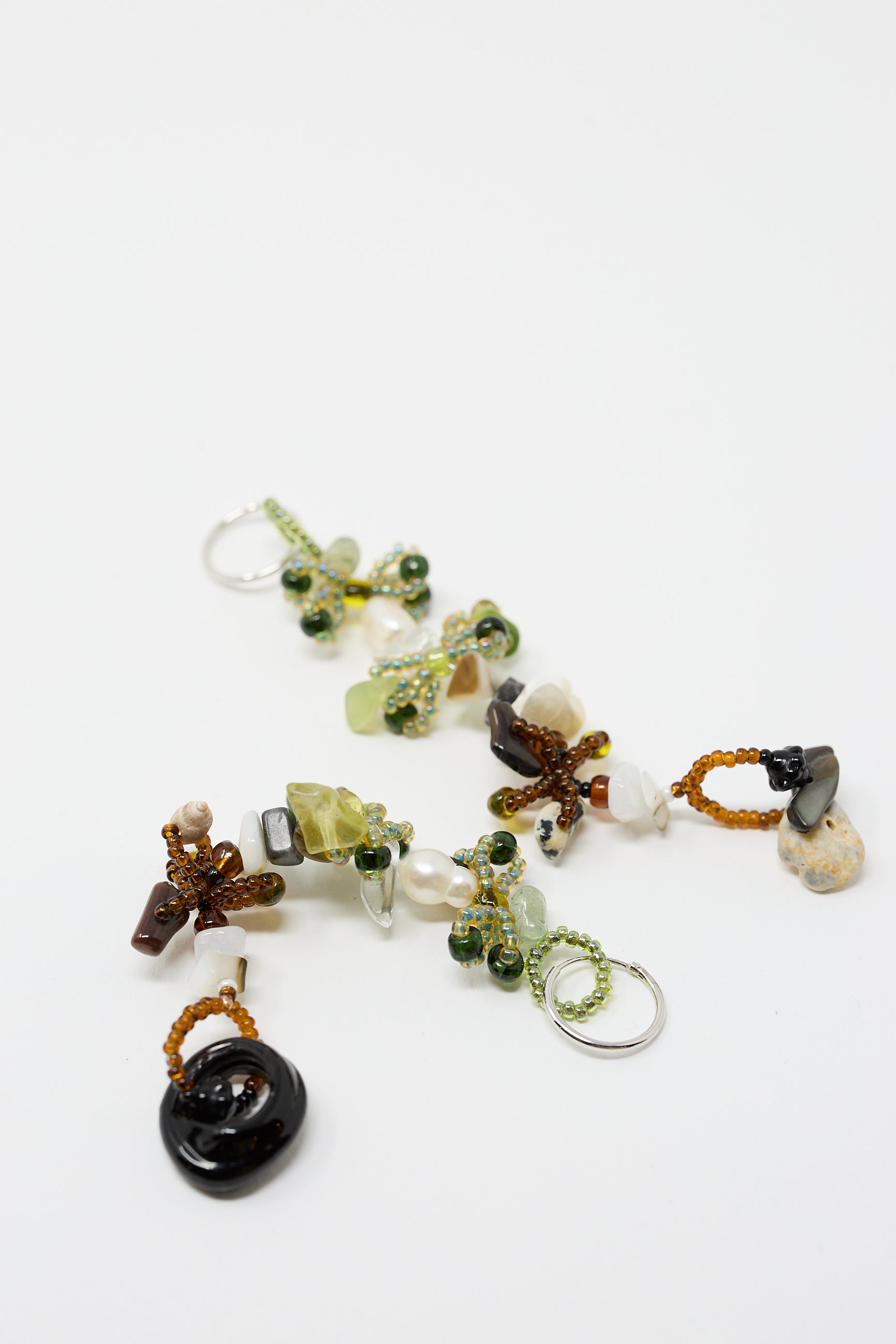 A pair of intricate Harvest Earrings 2.0 by Yona Kohen featuring various glass beads and stones arranged in clusters on sterling silver hoops, laid out on a white surface.