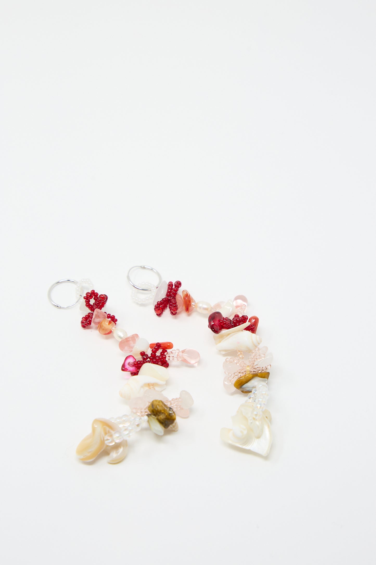 A pair of Kiraz Earrings by Yona Kohen, featuring hand-beaded elements with small red, pink, and white beads on sterling silver hoops, lying on a white surface.