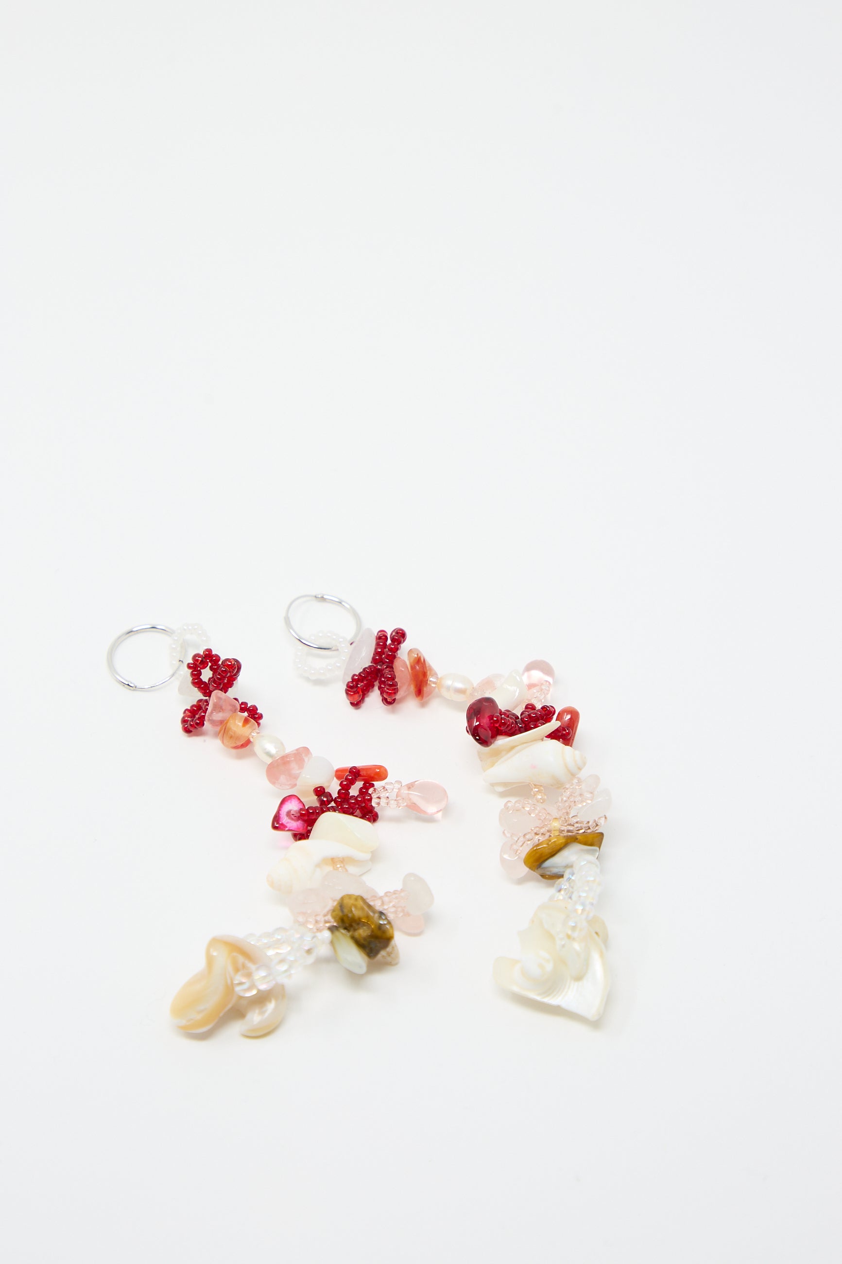 A pair of Kiraz Earrings by Yona Kohen, featuring hand-beaded elements with small red, pink, and white beads on sterling silver hoops, lying on a white surface.