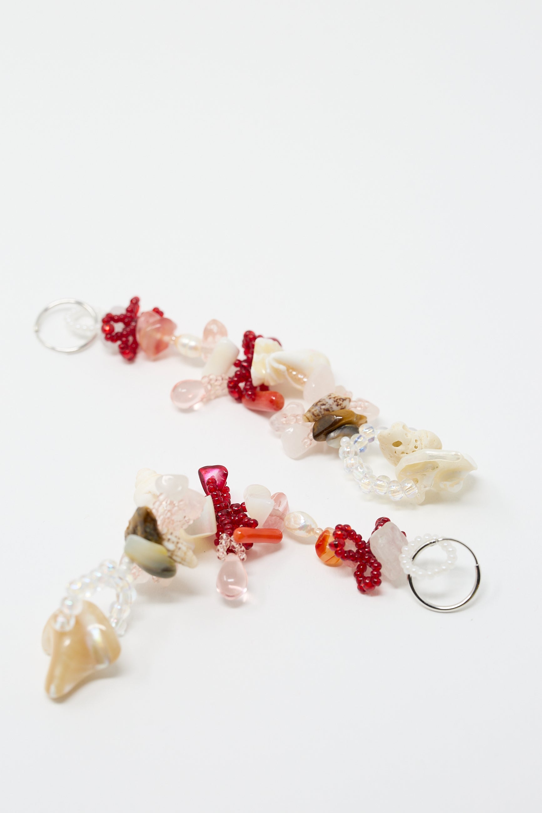 Two Kiraz Earrings by Yona Kohen featuring assorted stones, pearls, and coral in shades of red, pink, and white, arranged on a plain white background. Crafted with attention to detail, these unique accessories highlight locally sourced materials.