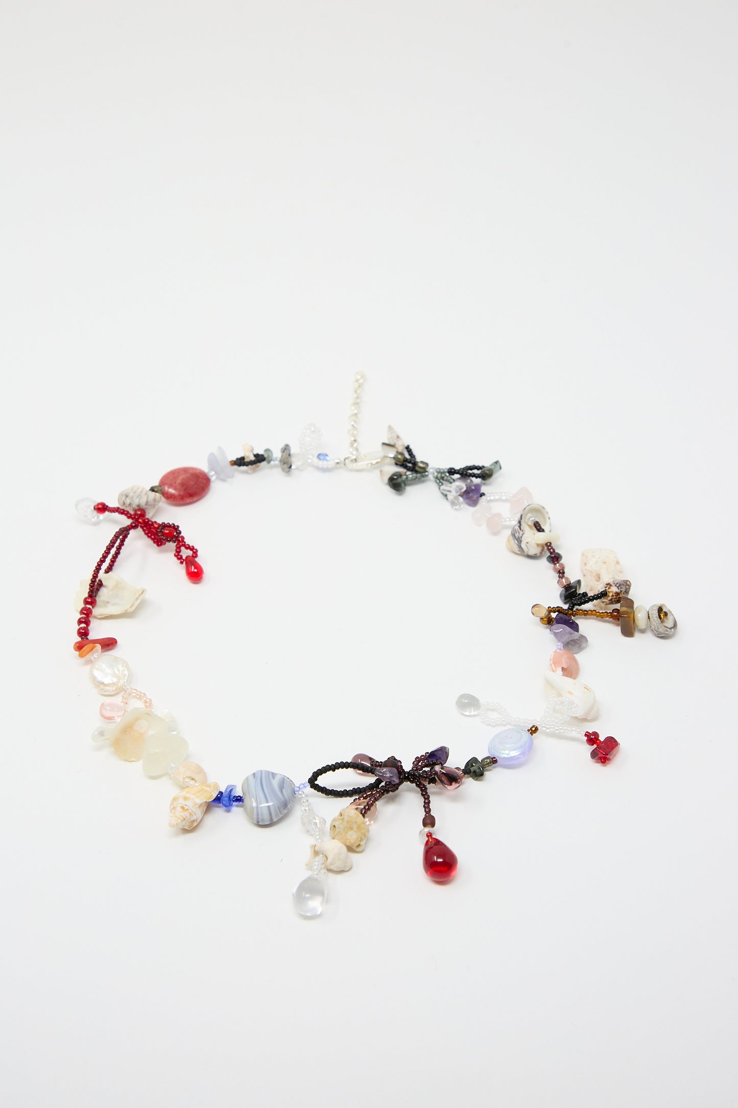 The Love is Stronger Than Pride Necklace by Yona Kohen is a vibrant, hand-beaded piece made of assorted glass beads and semi-precious stones. Featuring various shapes and colors arranged in an uneven pattern, it is beautifully displayed on a plain white background.