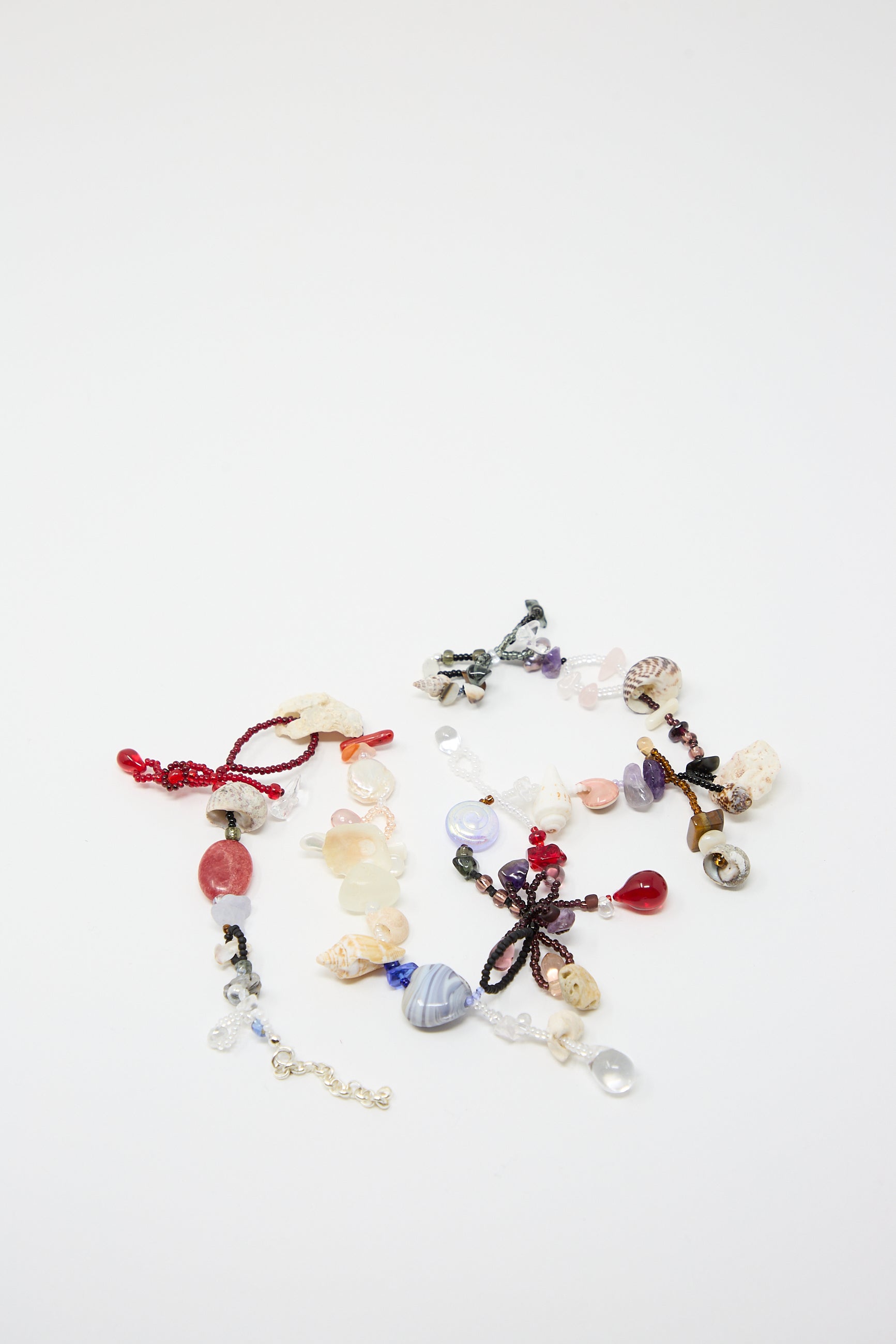 Three elegant "Love is Stronger Than Pride" necklaces by Yona Kohen, showcasing variously colored beads, some adorned with semi-precious stones and glass beads, beautifully arranged on a white surface.