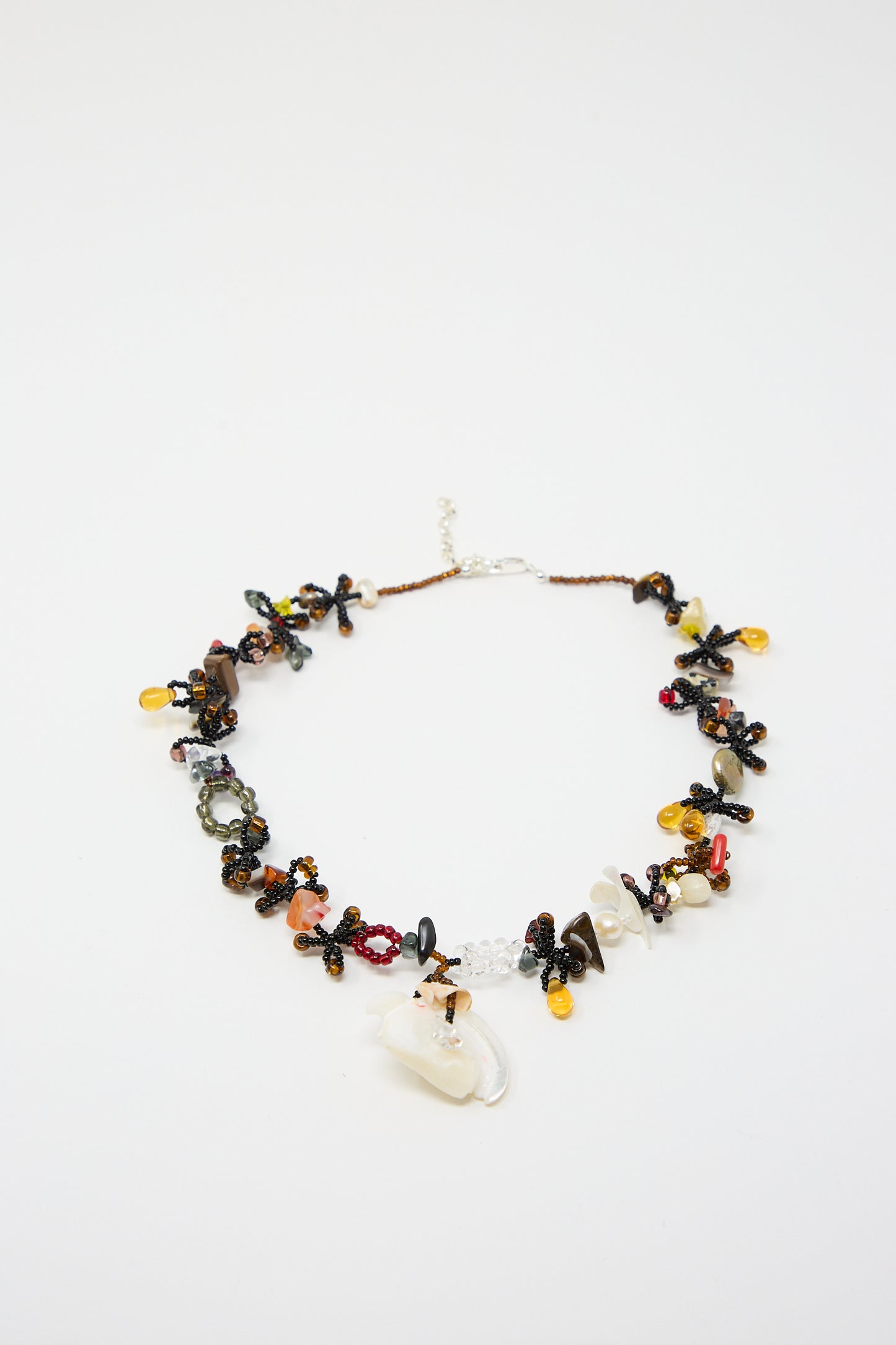 The Yona Kohen Silkworm Necklace in Black is a meticulously hand-beaded piece, showcasing a vibrant assortment of stones and materials such as amber, semi-precious quartz, dark crystals, and glass beads, elegantly arranged on a delicate chain with a silver clasp.