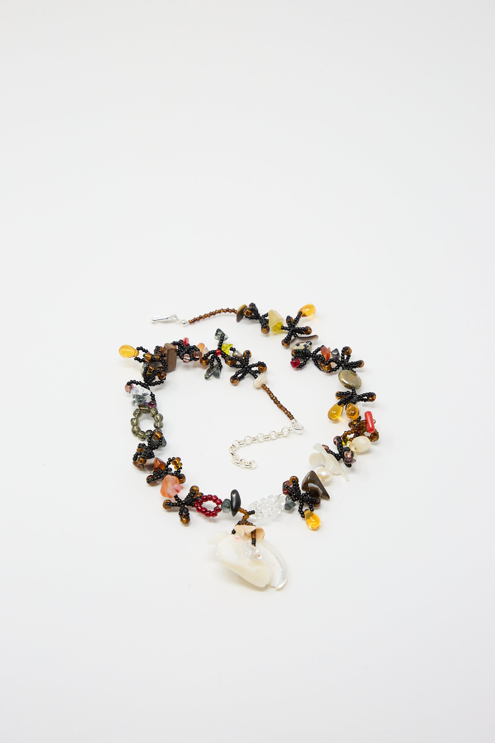 The Silkworm Necklace in Black by Yona Kohen is a colorful hand-beaded piece featuring a blend of semi-precious stones, various glass beads in red, yellow, and brown hues, and intricate floral designs. It includes a lobster clasp and chain extender on a white background.