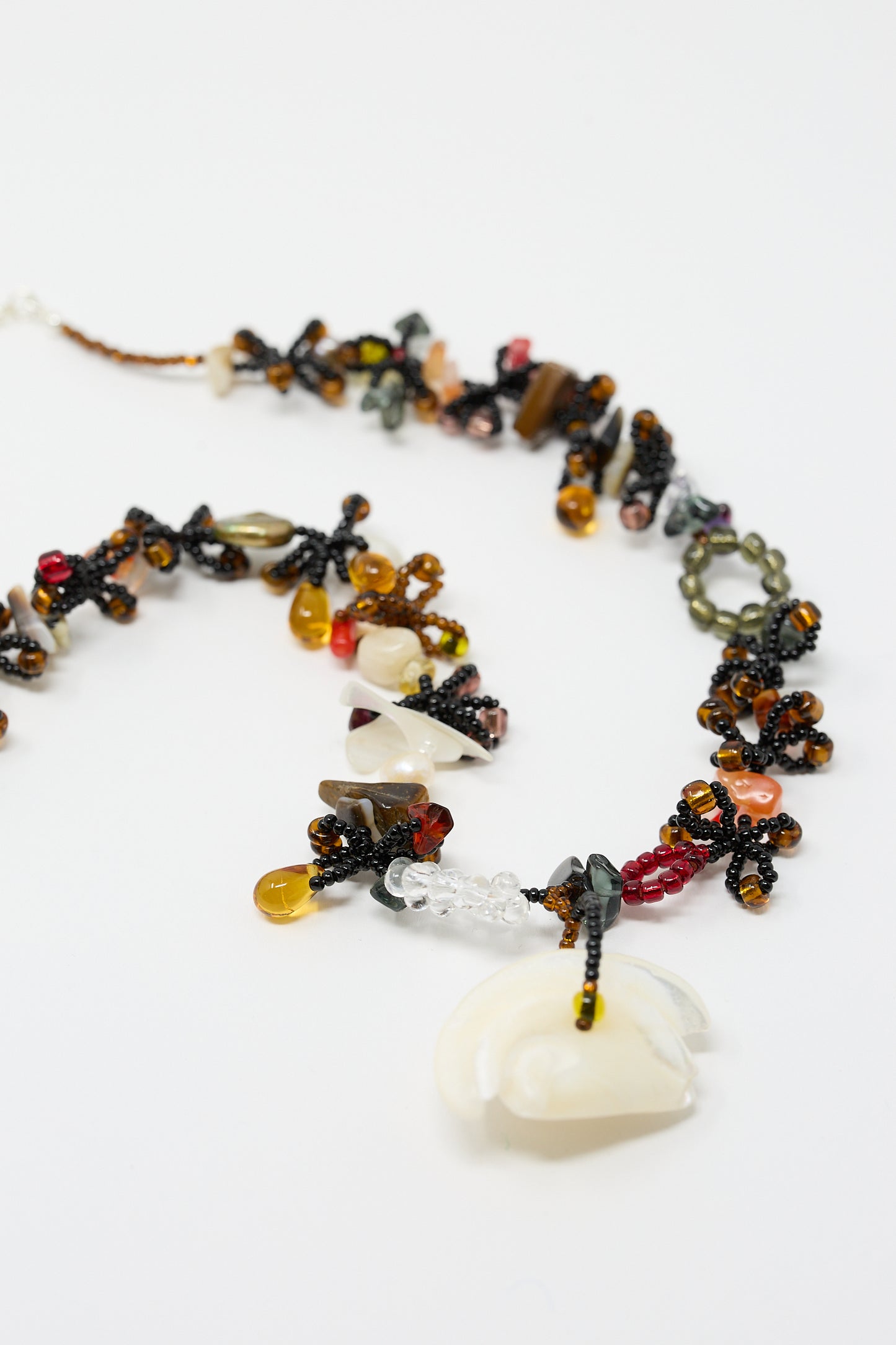 A close-up of the intricate Silkworm Necklace in Black by Yona Kohen, showcasing a stunning array of variously shaped glass beads and semi-precious stones in black, amber, red, and clear colors.