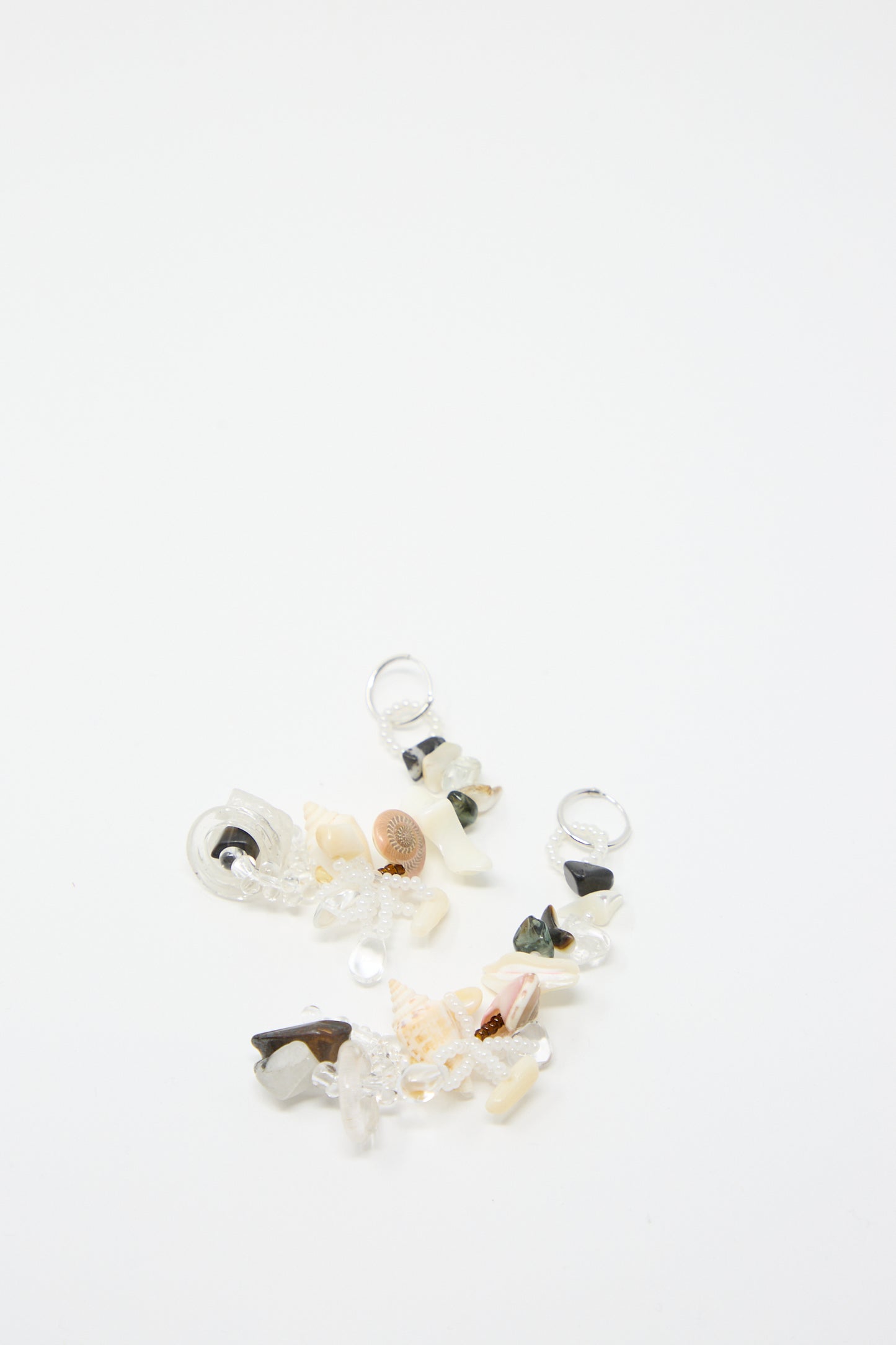 The Swamp Earrings by Yona Kohen, featuring a mix of small multicolored decorative elements, including natural stones, pearls, and glass beads, laid on a white background.