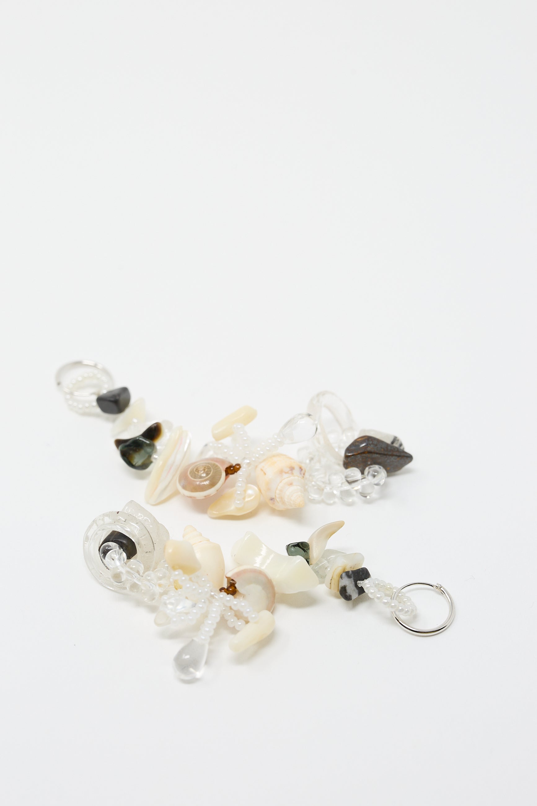 A pair of Swamp Earrings by Yona Kohen, showcasing various small, decorative beads and charms, including natural stones, crafted from white and black materials, elegantly displayed on a white background.