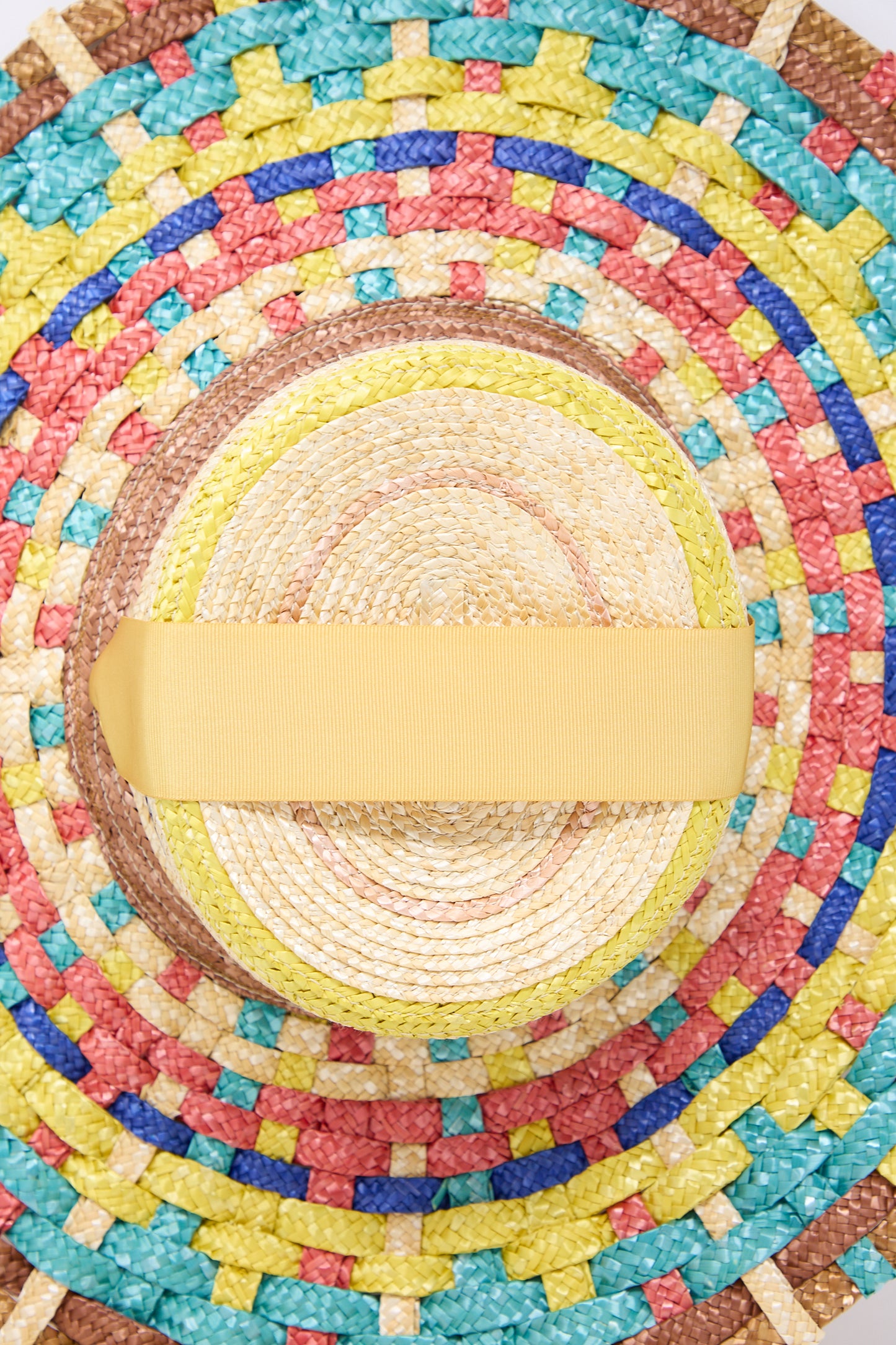 Top view of a colorful handmade Straw Cuchi Tris-Tras No. 94 Hat with Laces by Zahati featuring a wide yellow ribbon, with a pattern of concentric circles in blue, green, red, and natural braided straw colors.